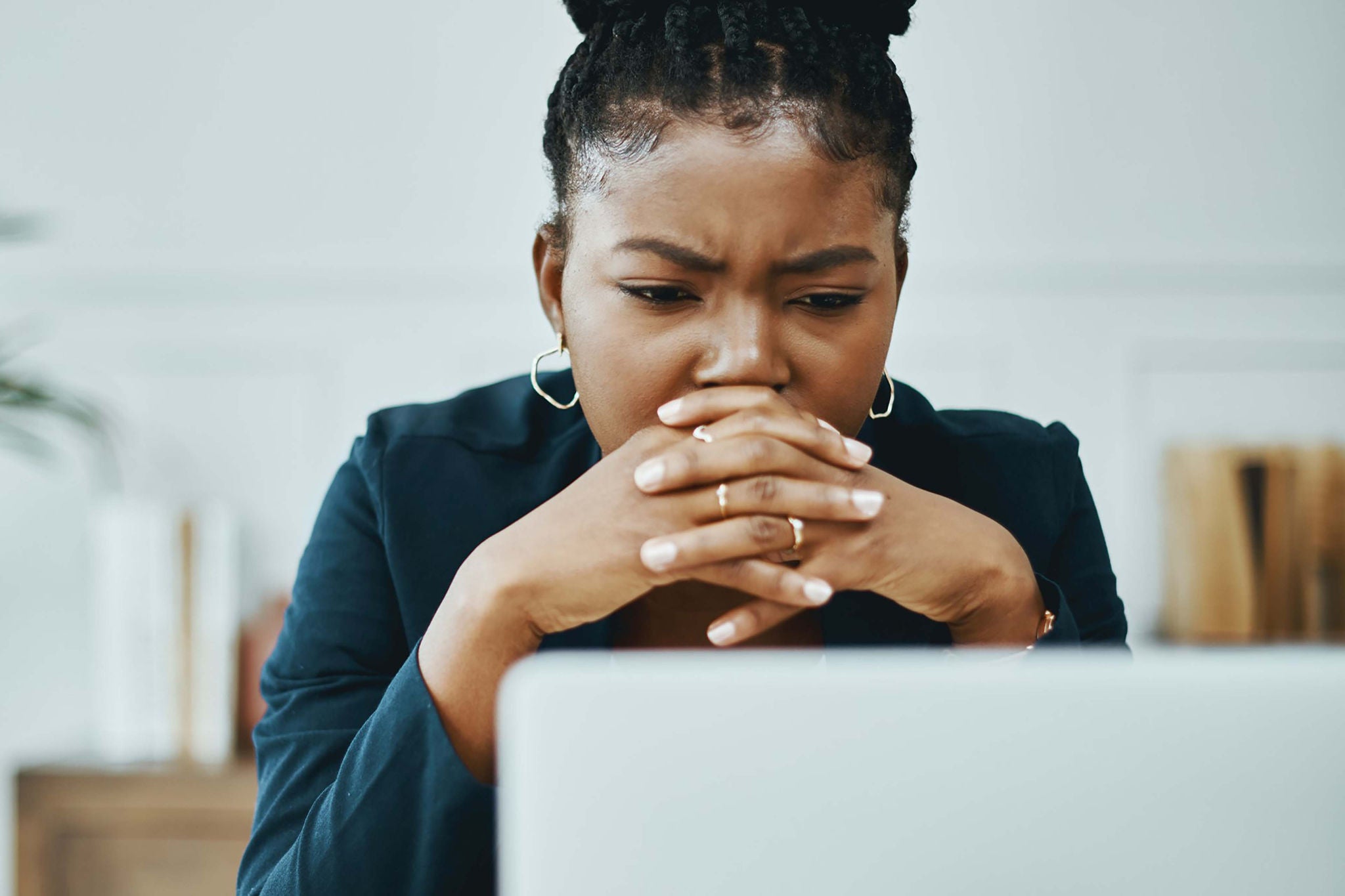 A person seated at a desk appears to be thoughtfully engaged while working on a laptop.