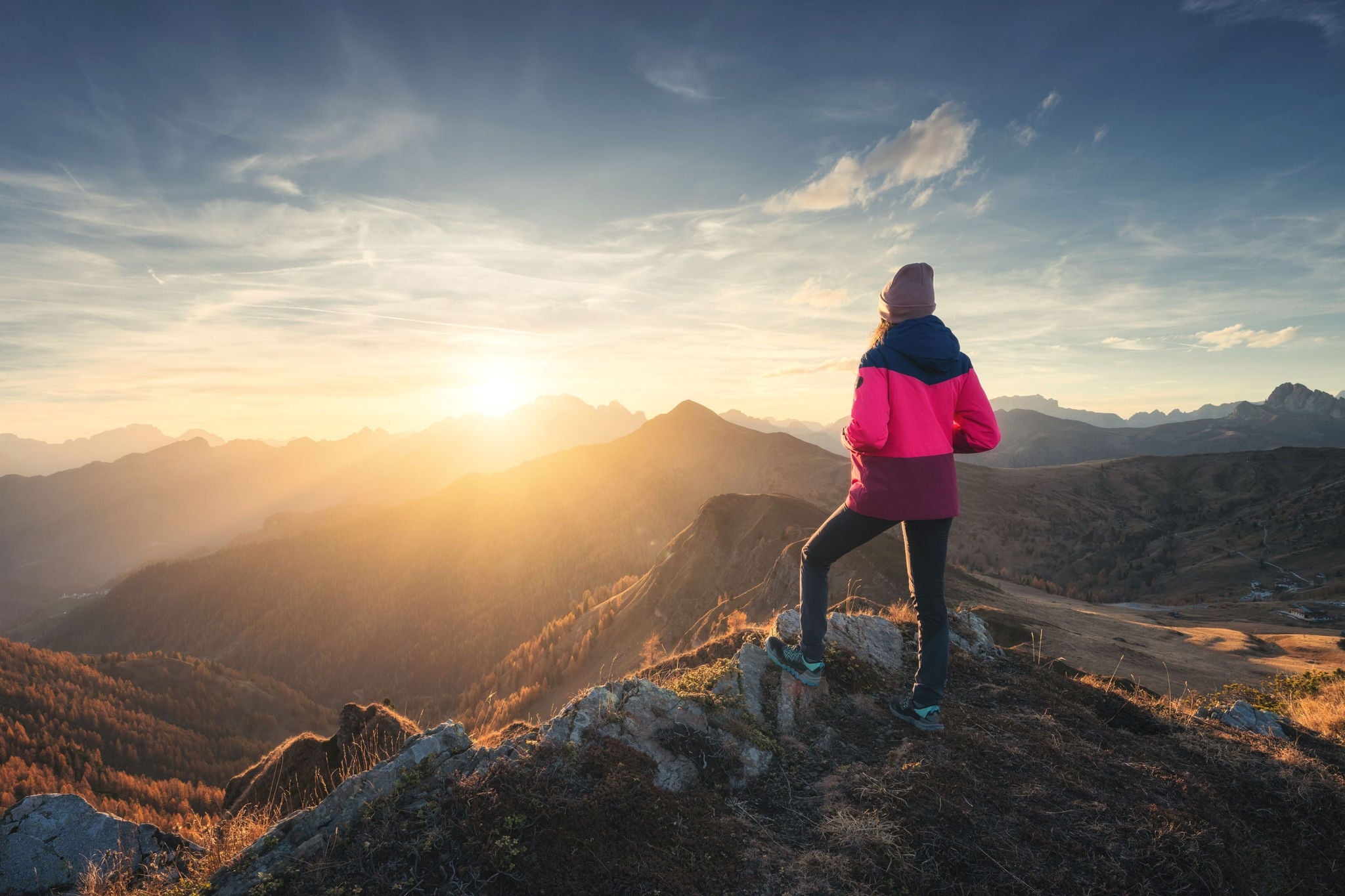 Wandernde Person steht auf Gipfel und blickt über Berglandschaft im Morgenlicht.