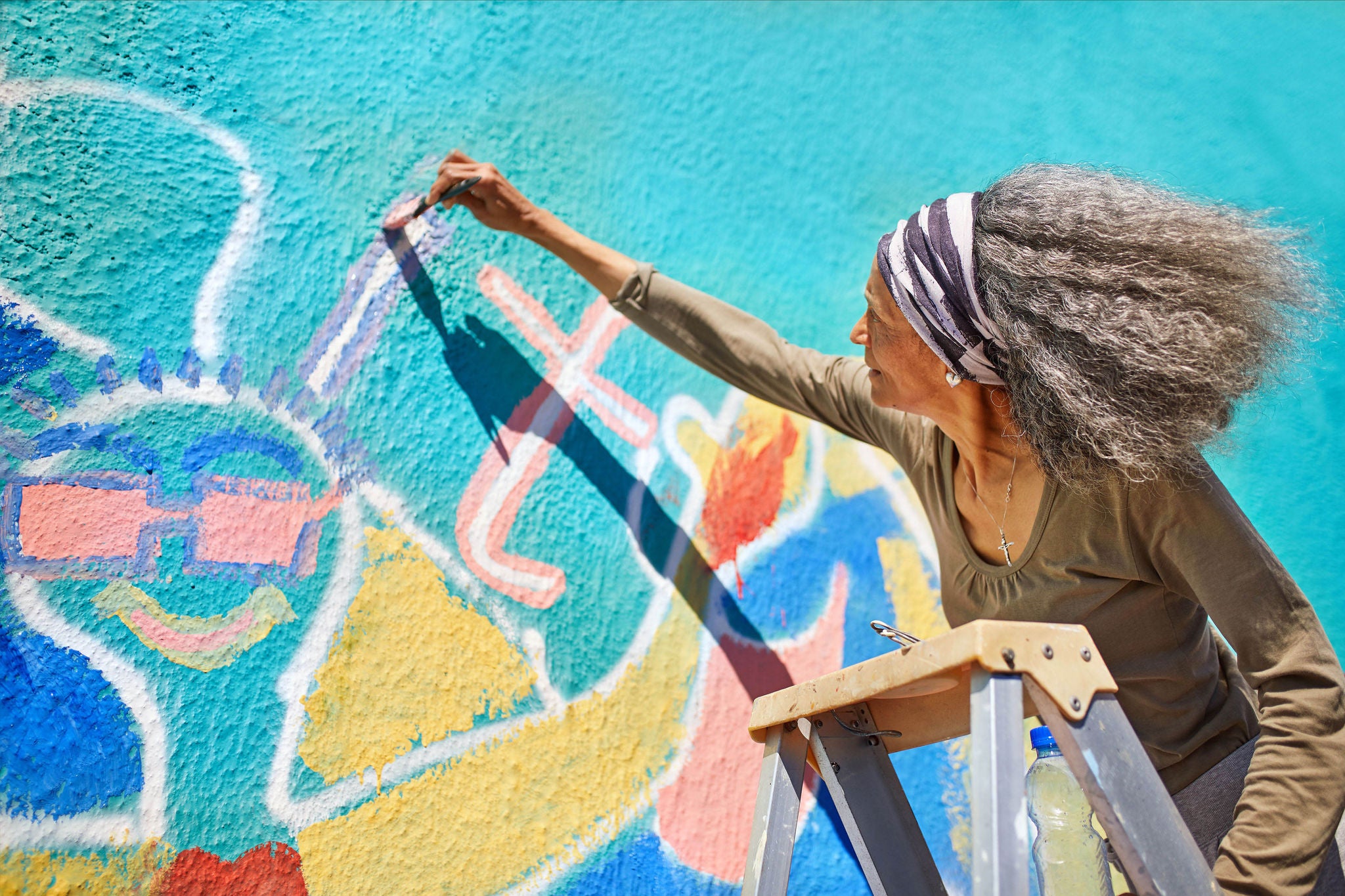 Senior woman painting vibrant mural on sunny wall