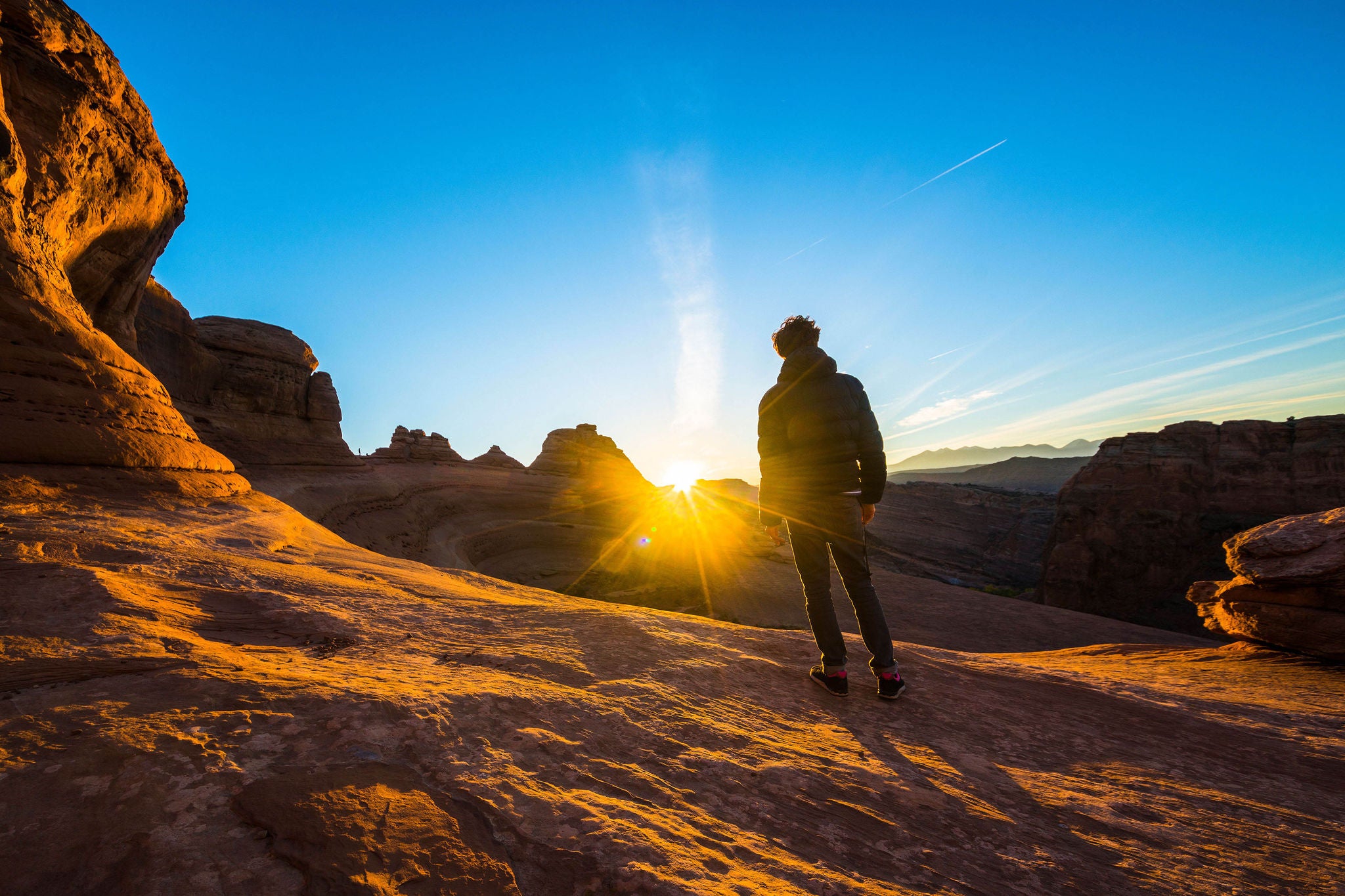The young hipster man, traveler and hiker, admiring the sunrise in the red canyon near by Delicate Arch at sunrise. The Arches National Monument, Utah, USA, North America. Unique geological formation.