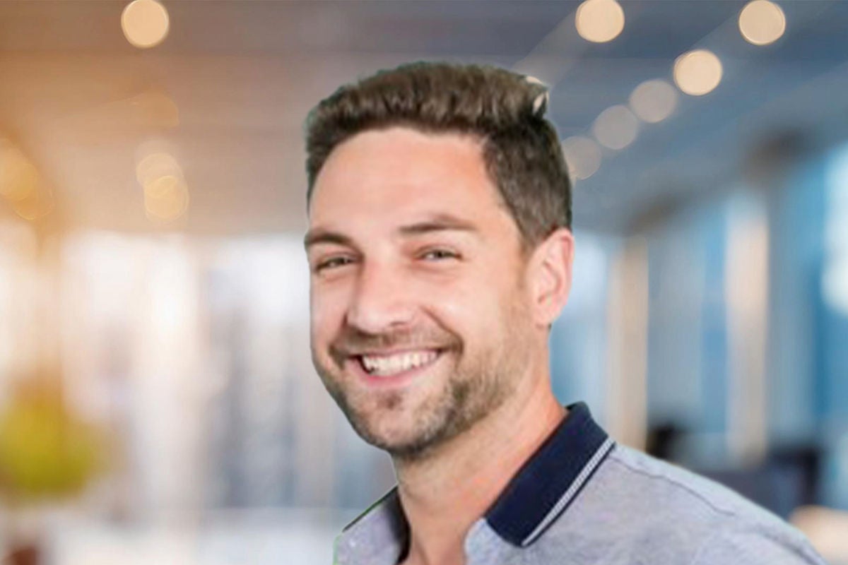 Eine Person in grauem Polohemd steht in heller Bürolandschaft mit weichen, warmen Lichtakzenten