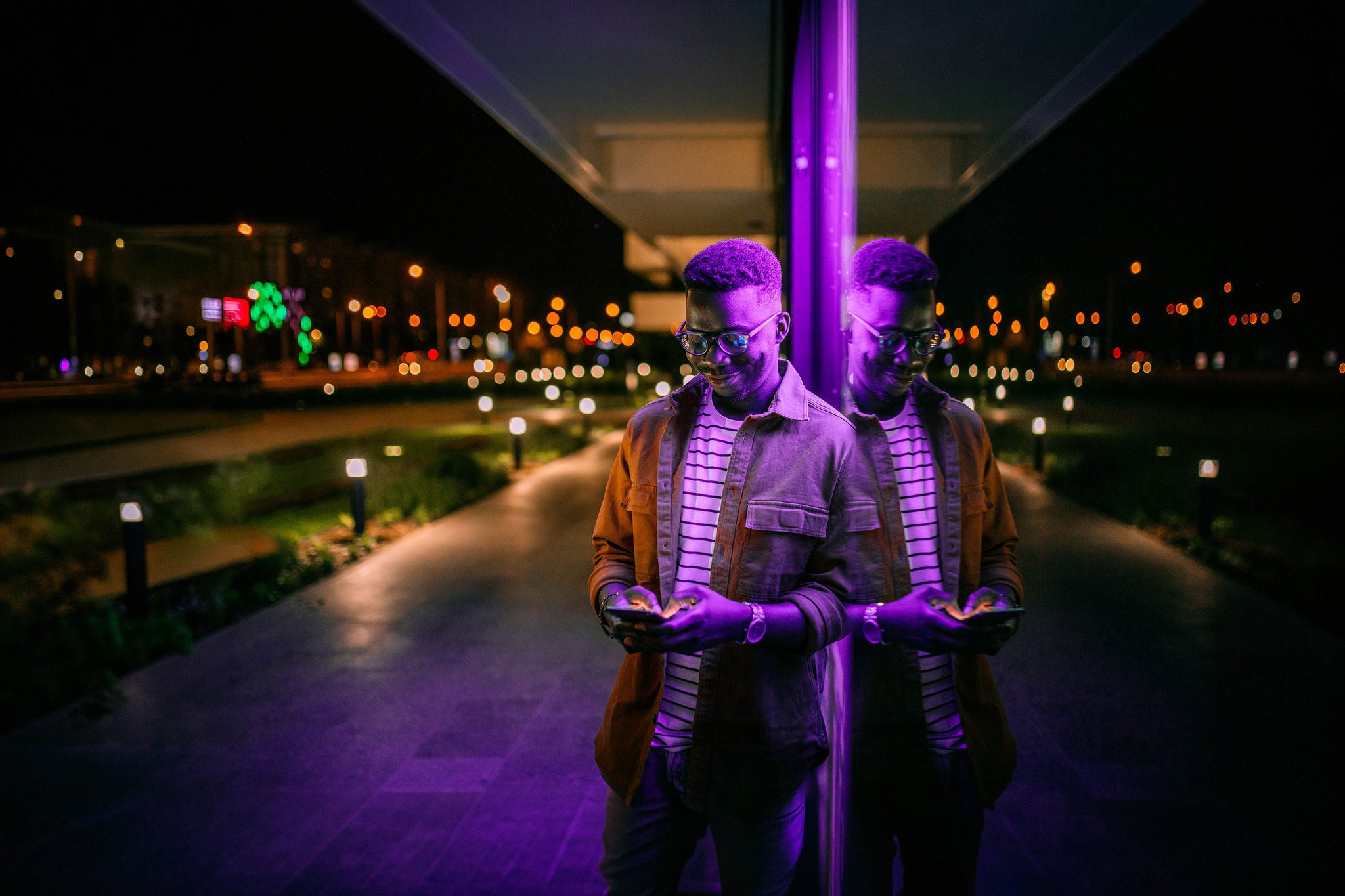 Young man using phone in front of neon lights on the street