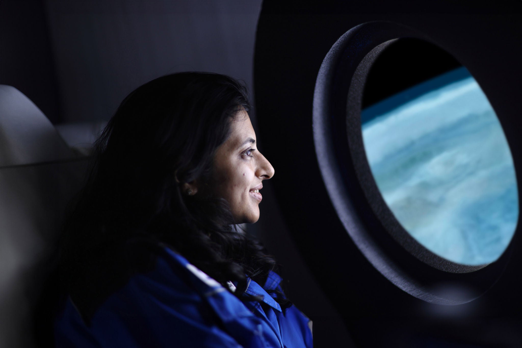 A commercial space traveler looking at the Earth through the window of a spaceship.