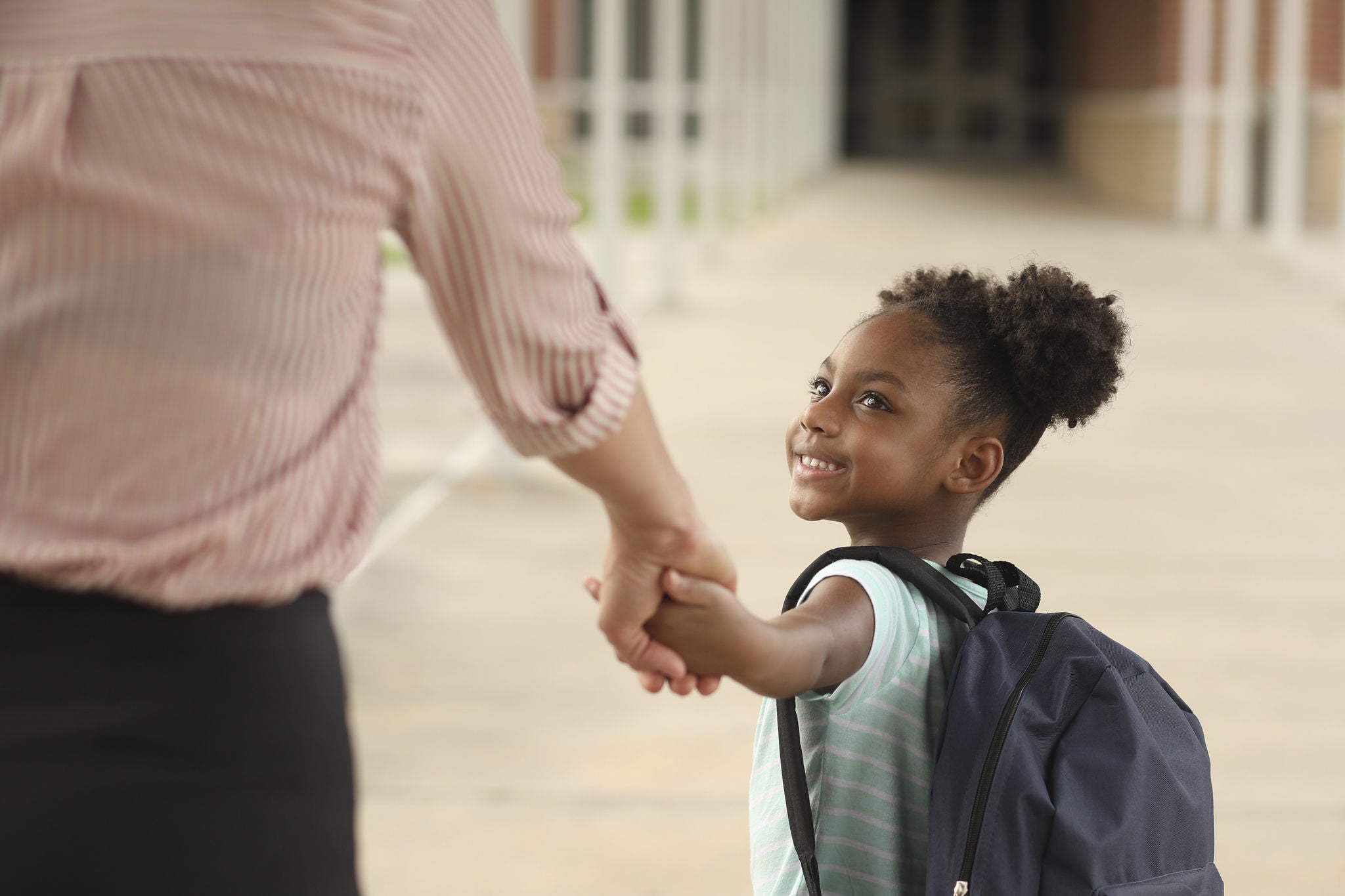 Girl and parent holding hands going to first day of school