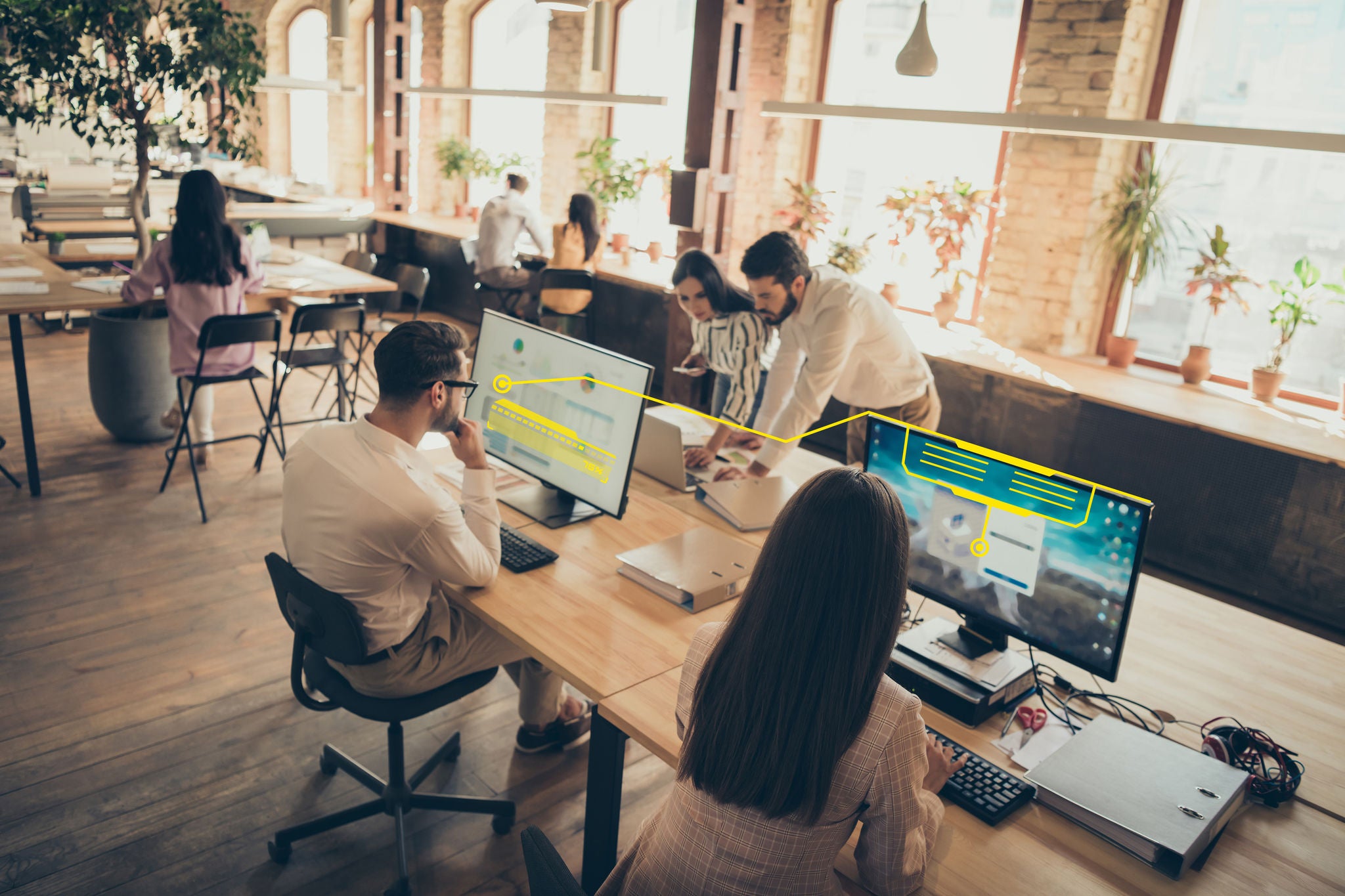 Professionals working together in an open office, analyzing data and digital insights displayed on desktop monitors.