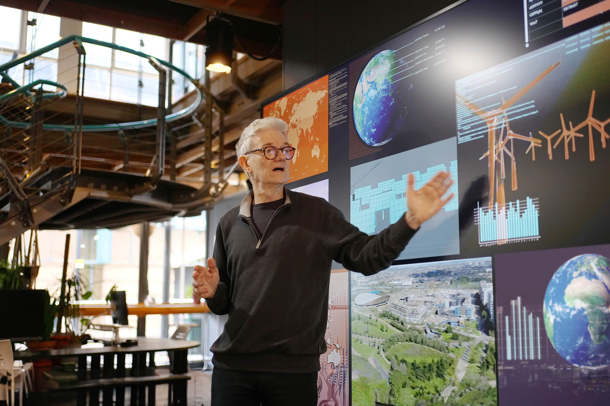 Stock photograph of a mature man giving a lecture beside a large movie screen.
He's showing images on a large screen related to modern energy production, ie sustainable energy.