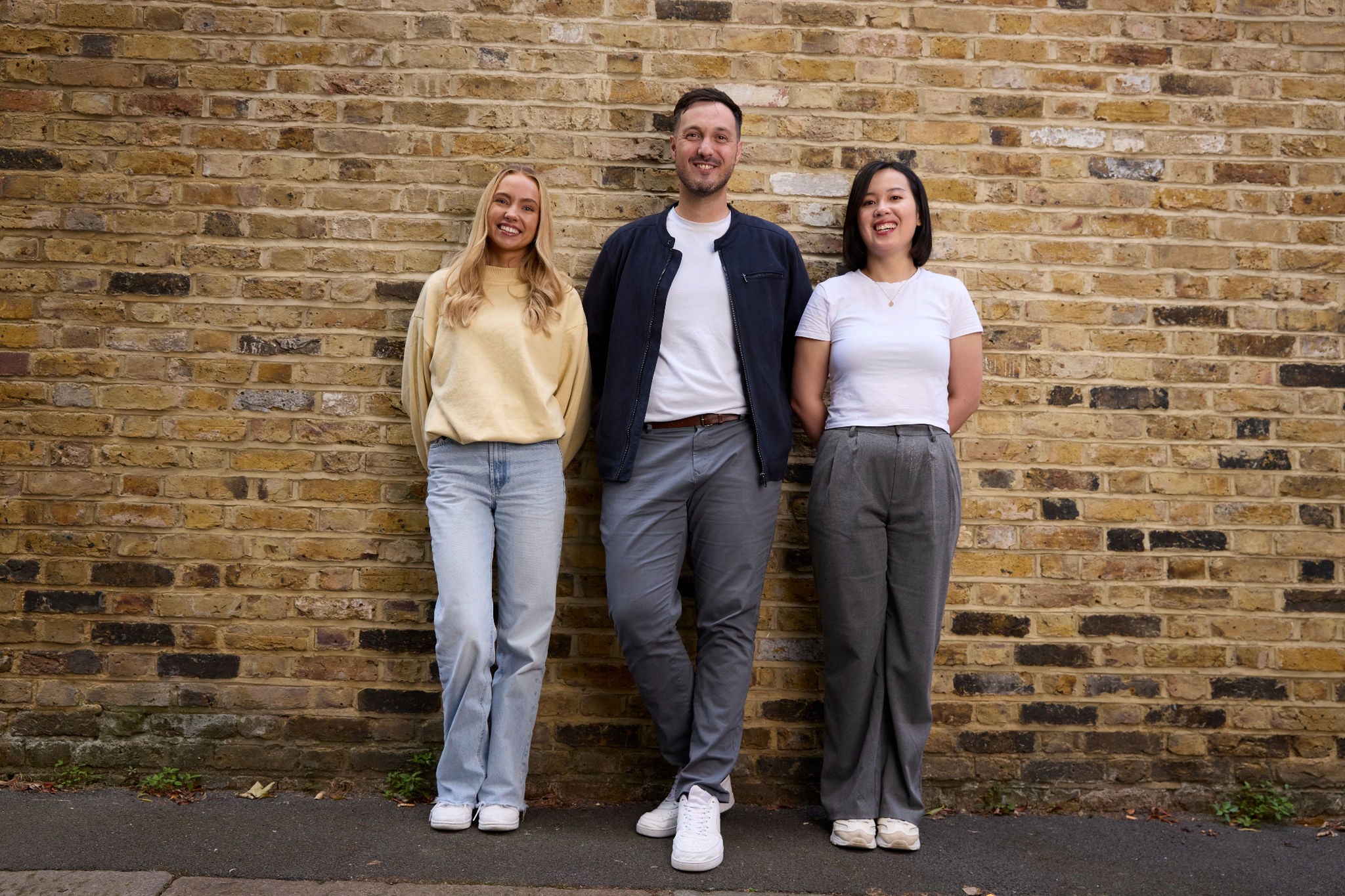Three colleagues posing together by a brick wall