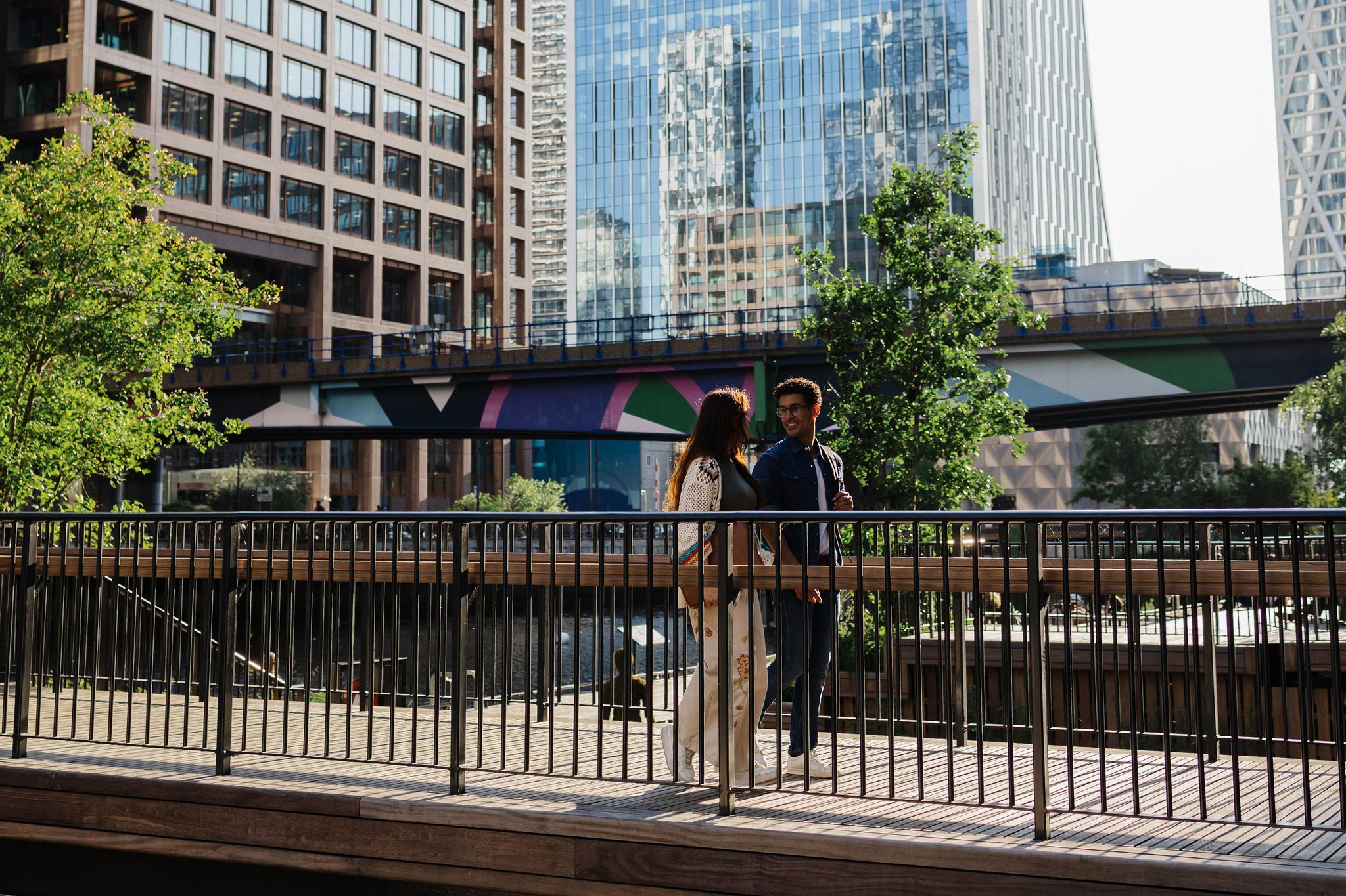 Two people standing on a walkway in a modern city with tall buildings around them