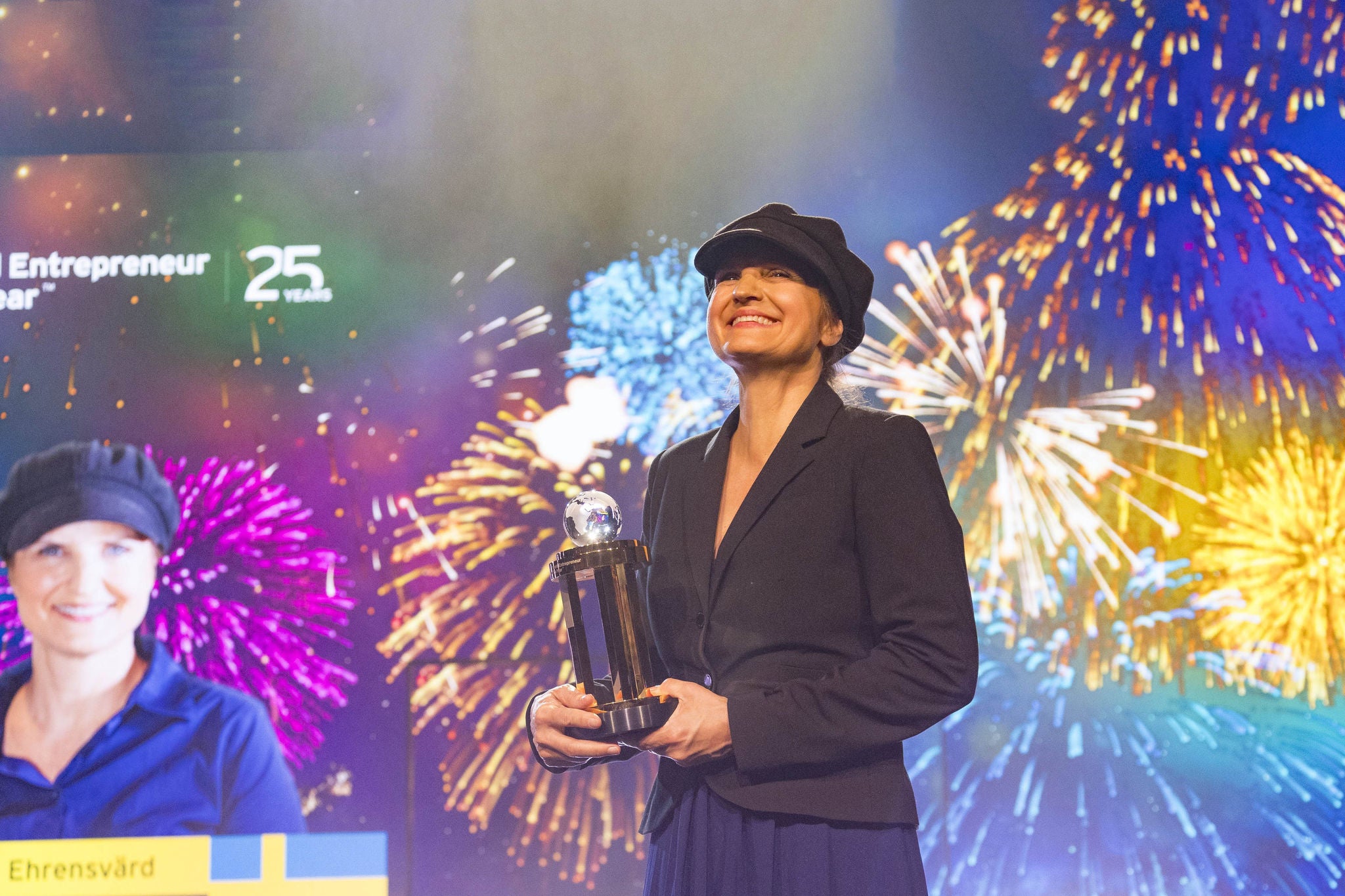 Stina Ehrensvärd på scen håller en trofé medan färgstarka fyrverkerier lyser upp bakgrunden vid WEOY ett evenemang