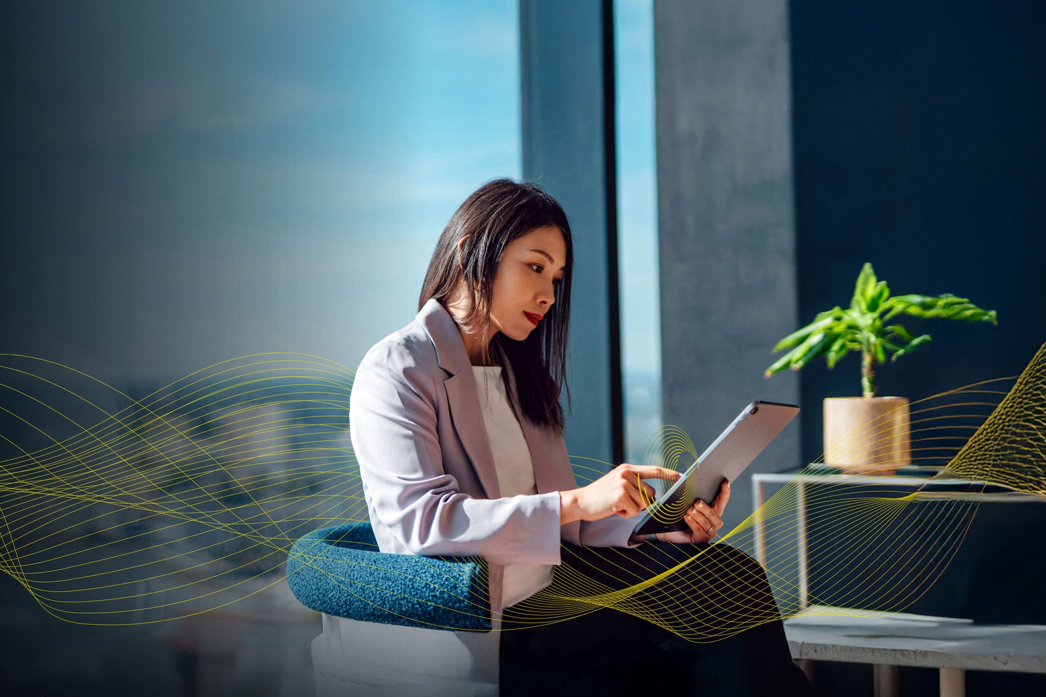 Asian woman sitting near window with blue walls and tablet in her hands