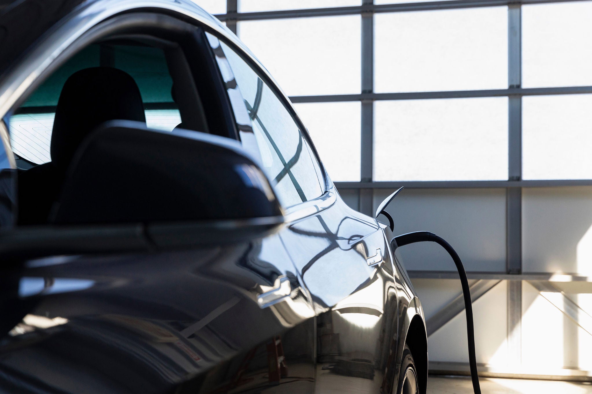 Closeup of an electric car parked indoors with a charging cable connected. A garage door is visible in the background.