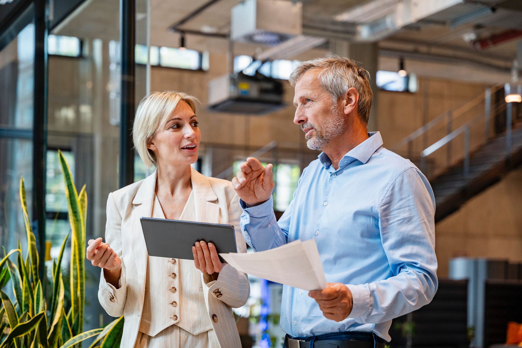 Colleagues discussing business in a modern office holding tablet and papers