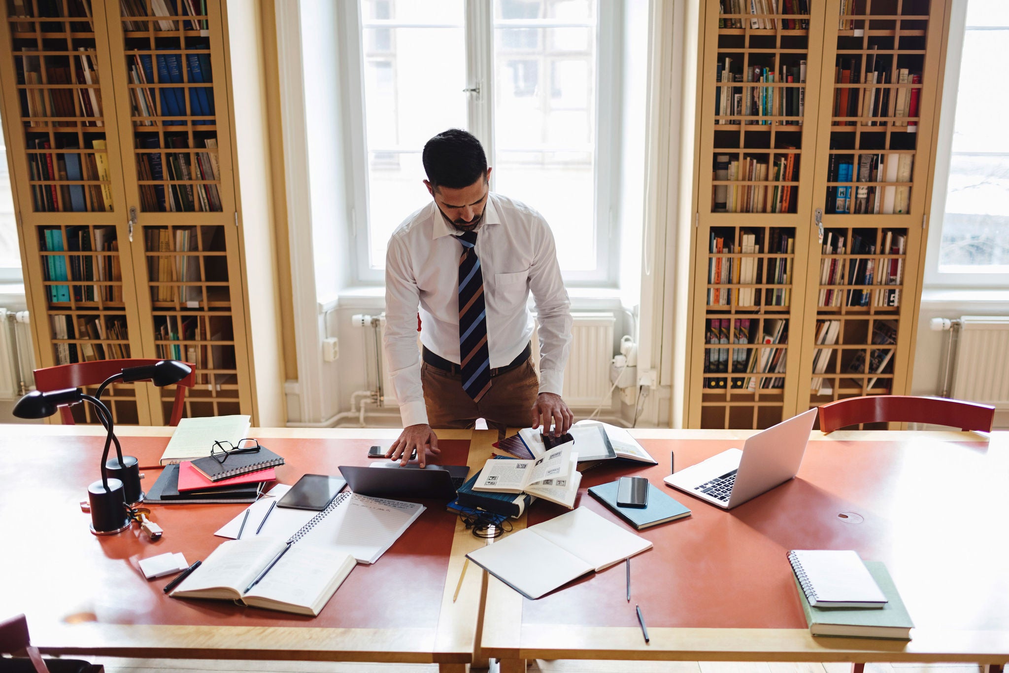 Man working at a table with books and a laptop in a library