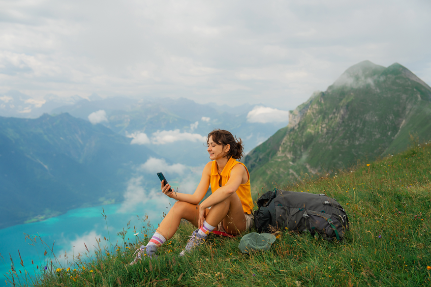 EY PARTHENON USE ONLY’-Woman sitting on the meadow in Swiss Alps using smartphone during the hike