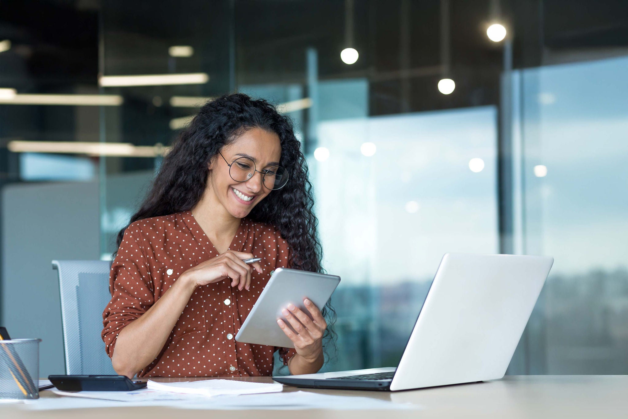 Frau arbeitet im Büro mit Tablet und Laptop