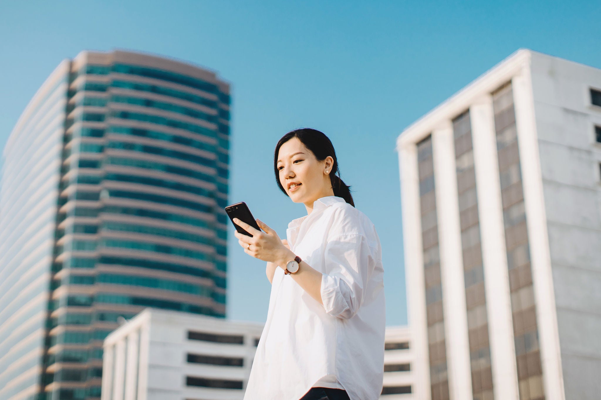 Young woman emailing on smartphone in city against highrise city buildings