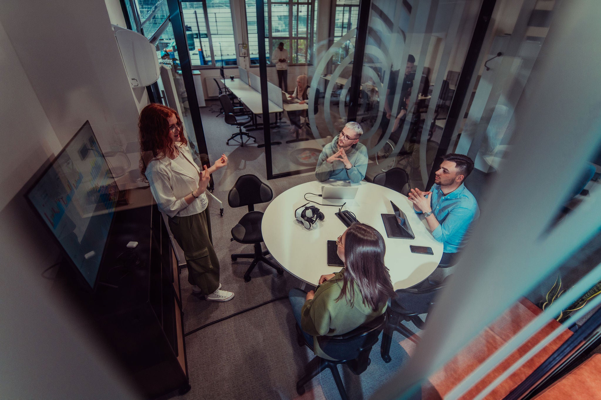 A group of young business entrepreneurs engages in a focused meeting, discussing various business strategies and collaboratively solving challenging problems, showcasing ambition, creativity, and teamwork in modern glass office.