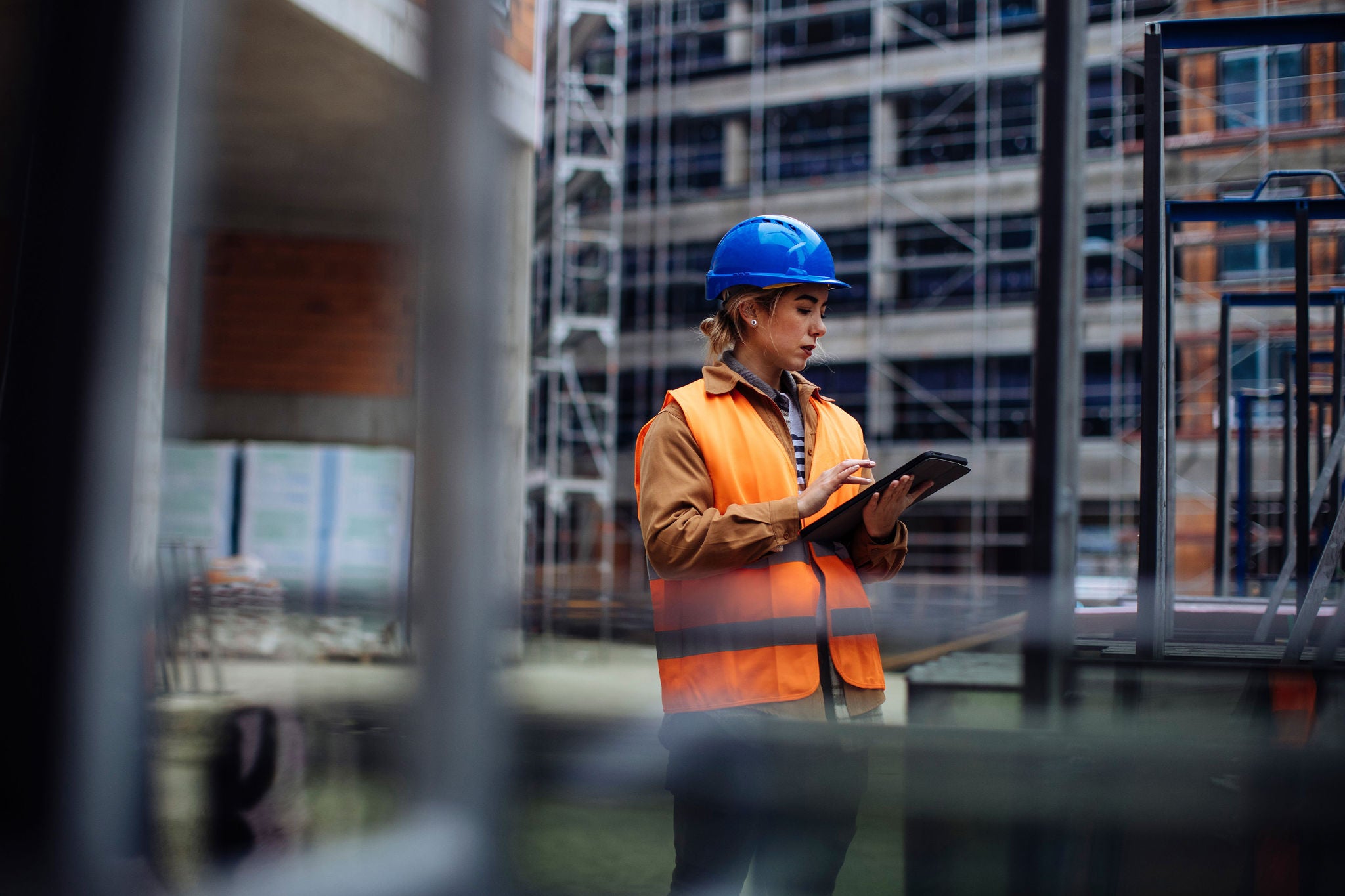 Fachkraft mit Schutzhelm und Tablet bei der digitalen Kontrolle auf einer modernen Baustelle.