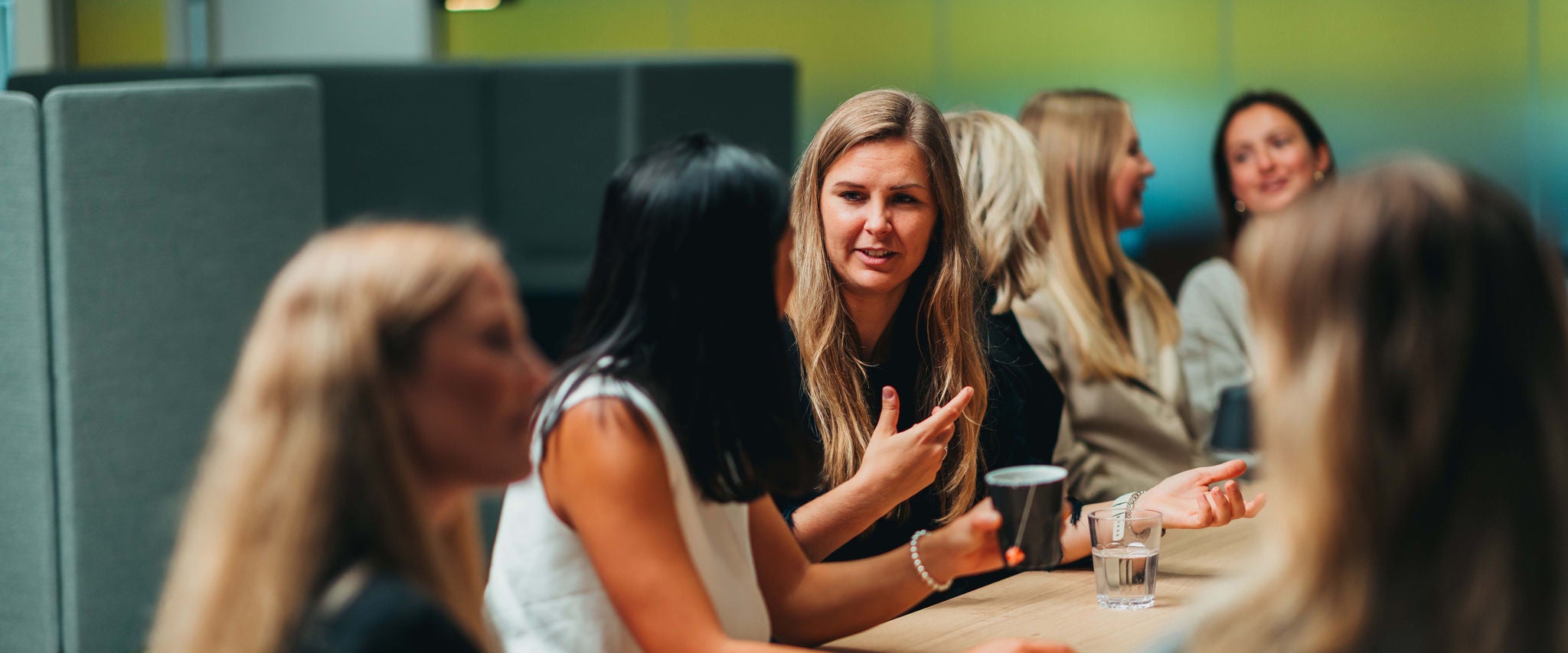 Colleagues sit around a table, engaged in discussion in a modern office setting.