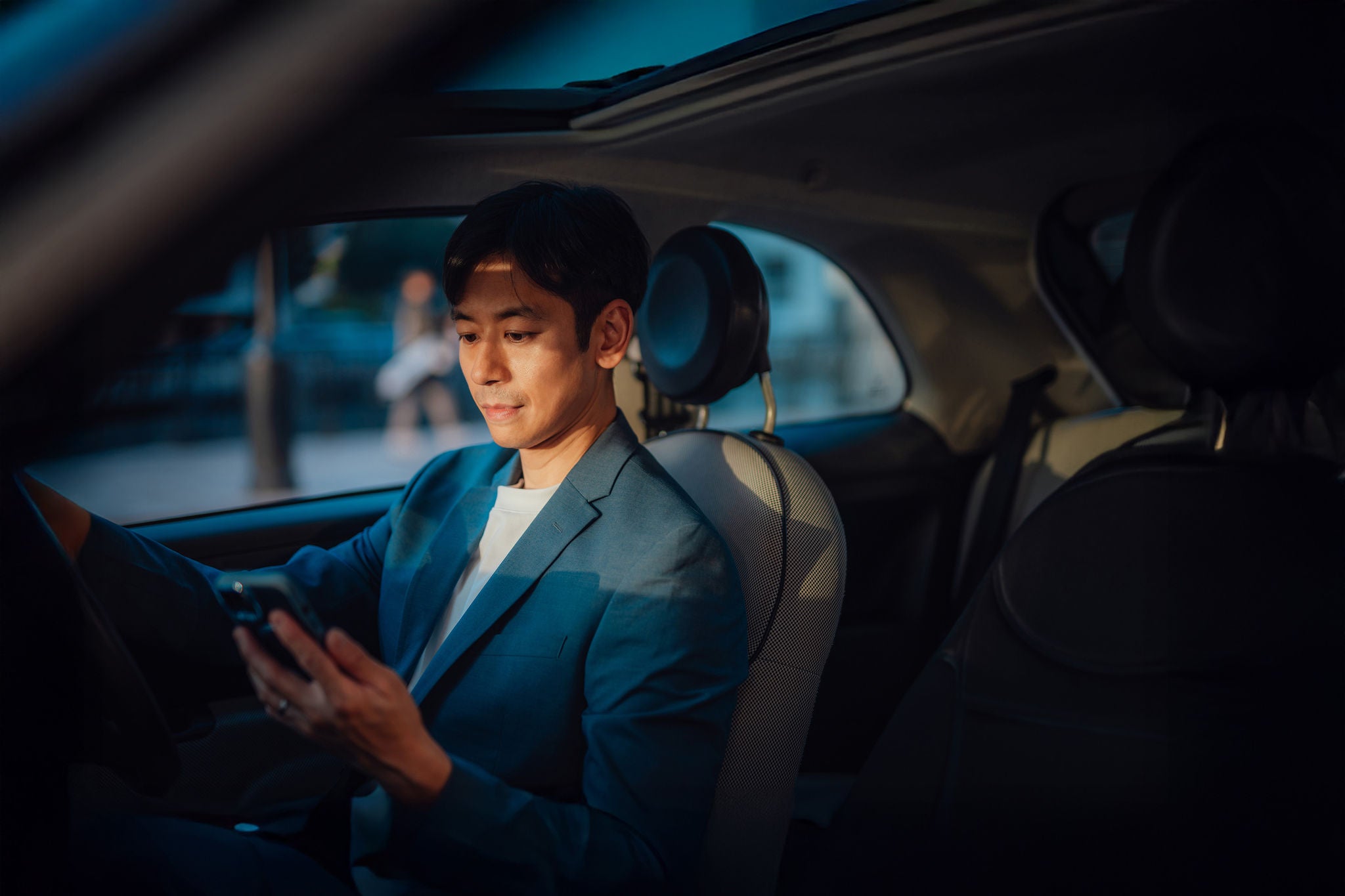 Asiatischer Unternehmer mit Smartphone im geparkten Auto