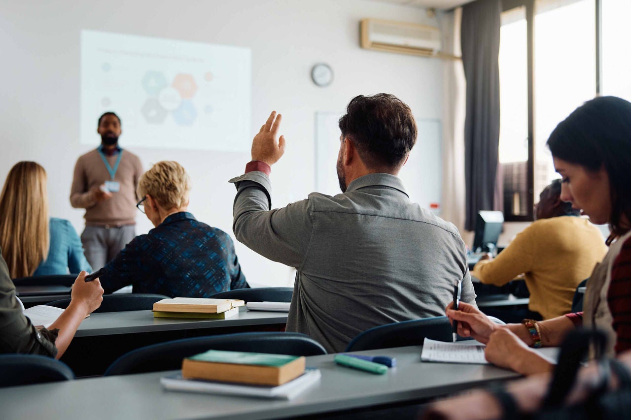 Person Writing on a Book By looking at his Laptop