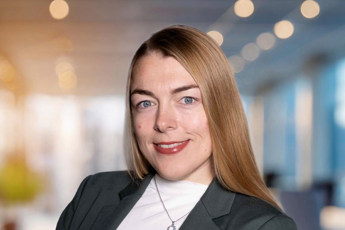 Eine Person steht in heller Büroumgebung, trägt ein dunkles Jackett und präsentiert einen gepflegten Auftritt