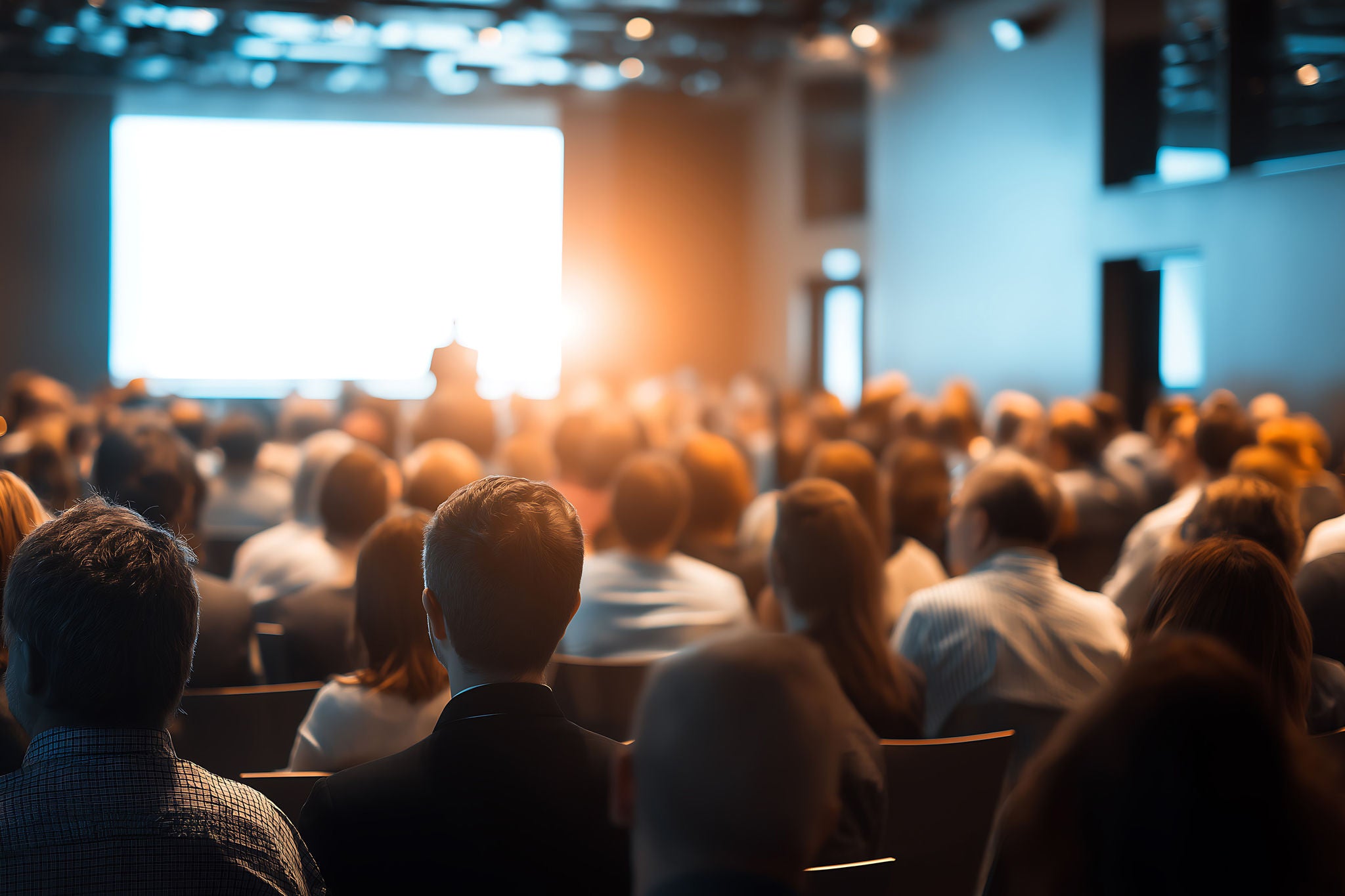 Publikum sitter i auditorium og ser på presentasjon på stor skjerm