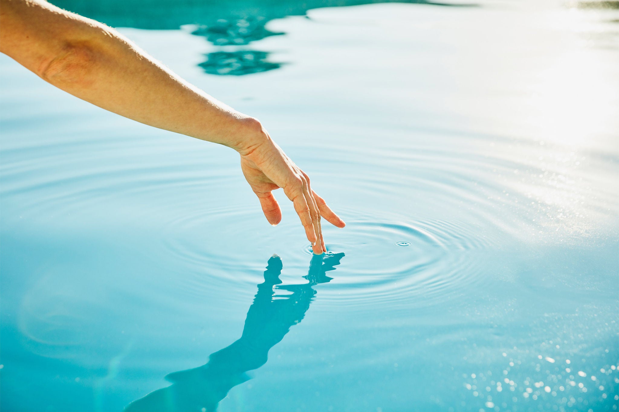 Close-up of a hand touching water, creating gentle ripples in a calm blue surface.