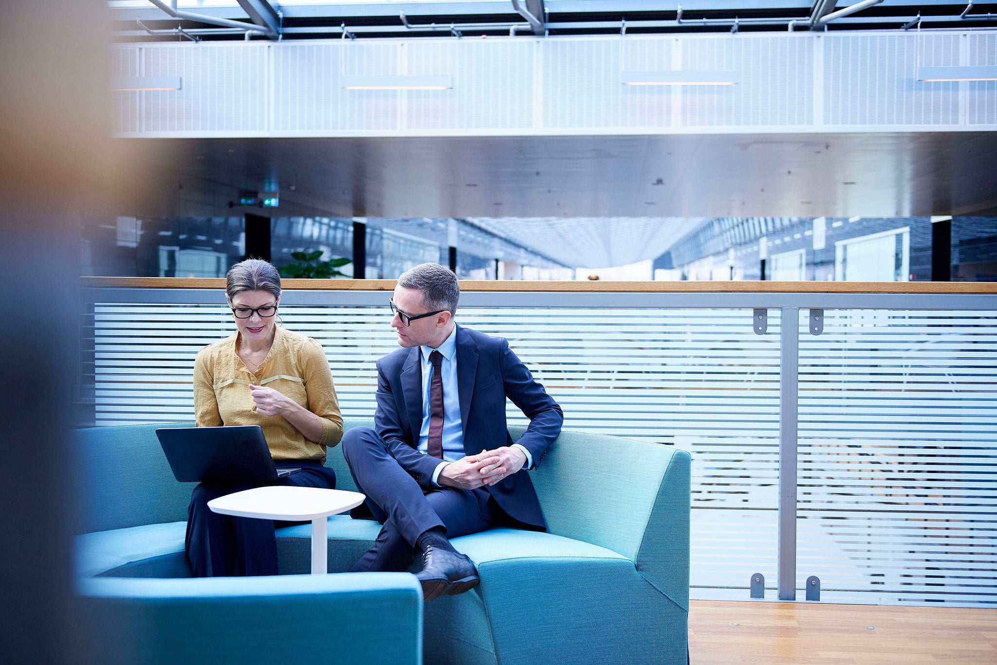 Liikemies ja nainen katsovat kannettavaa tietokonetta toimiston atriumissa