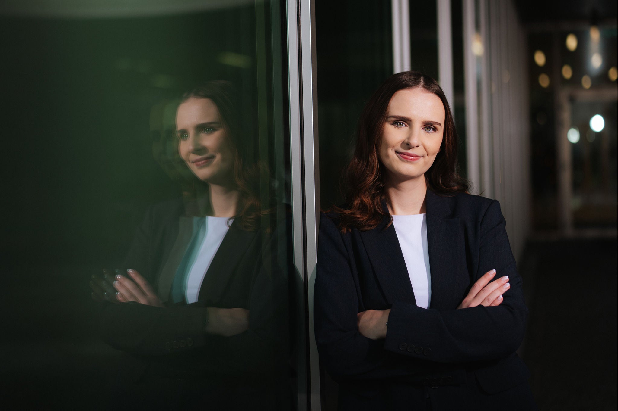Person in business attire standing with arms crossed near glass wall with reflection
