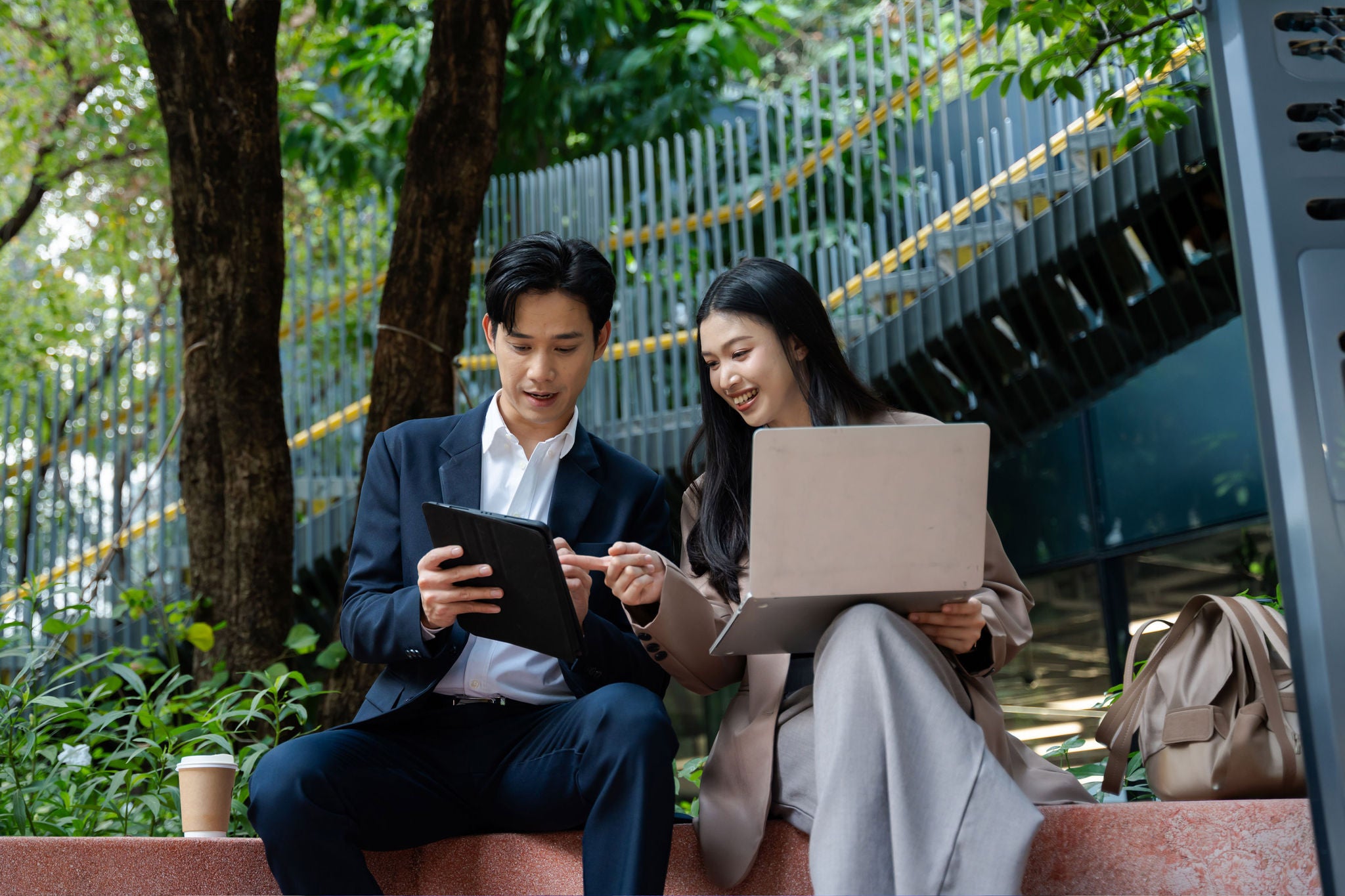 Diverse university students using laptops and tablets while studying together outdoors.