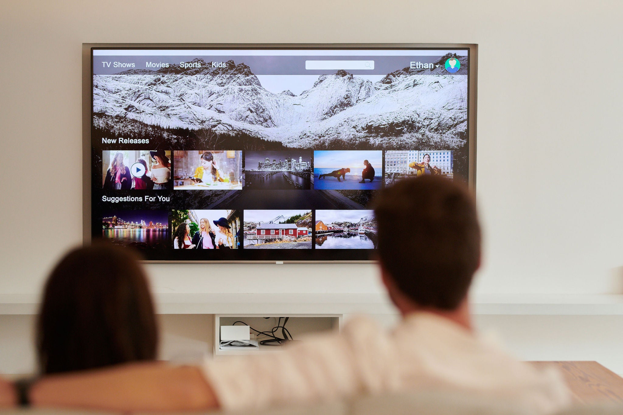 Selective focus of biggest screen of TV on wall and couple against on sofa.