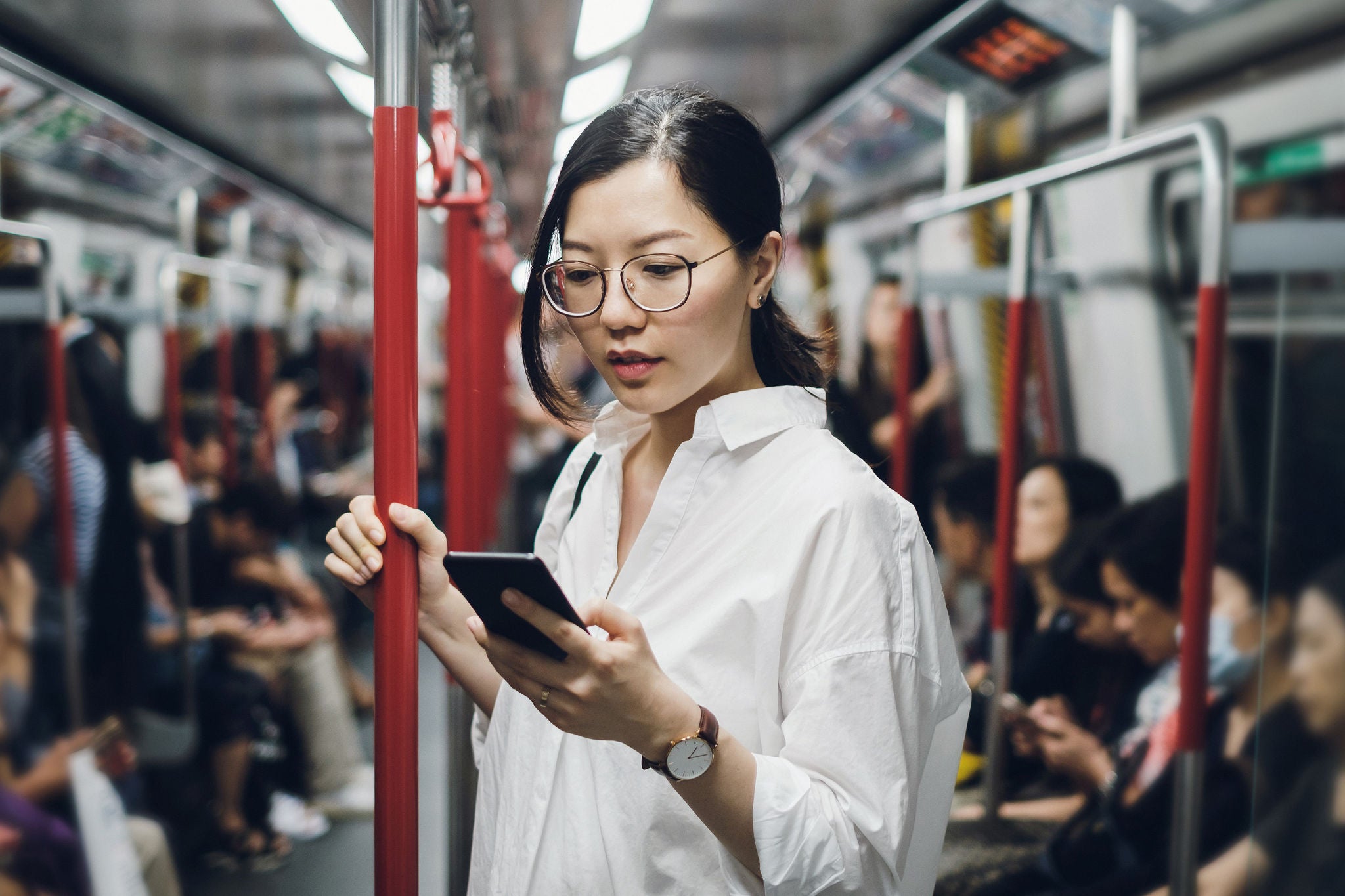 Asian woman in glasses checks phone on commute