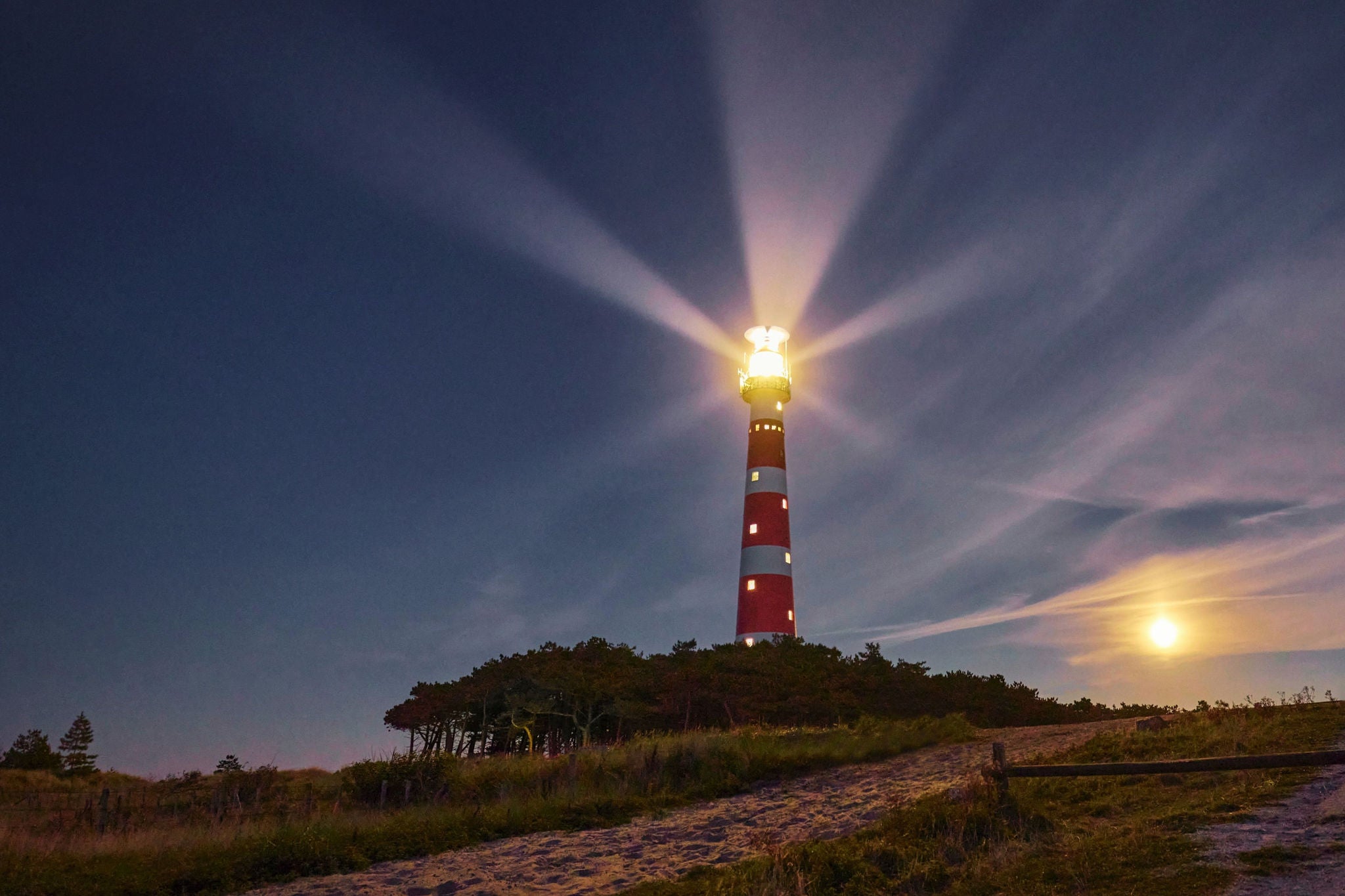 Phare diffusant des faisceaux lumineux la nuit sur paysage cotier