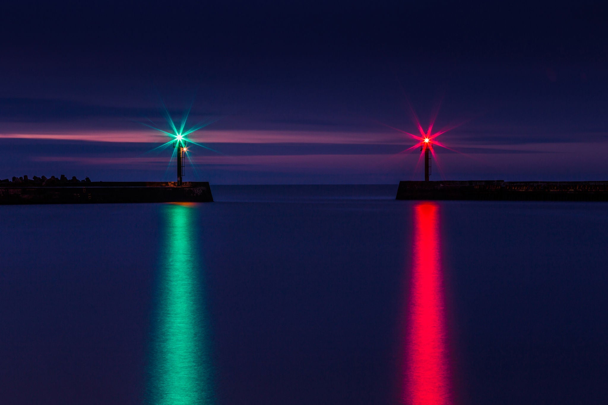Lights marking a harbour entrance reflected on the sea at dusk