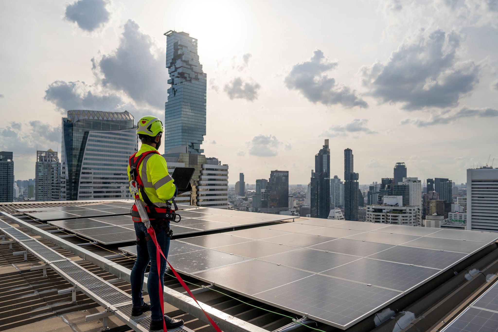 Blue collar worker checks solar cell panel. He works on the rooftop under sunlight. Hot weather and risk.