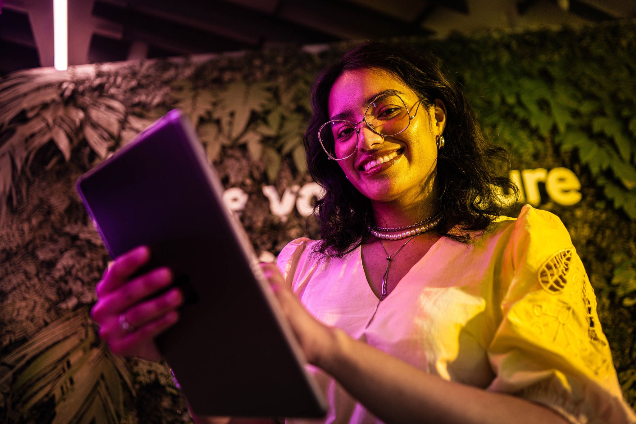 Mujer sonriente con lentes que mira a cámara con una tablet en la mano