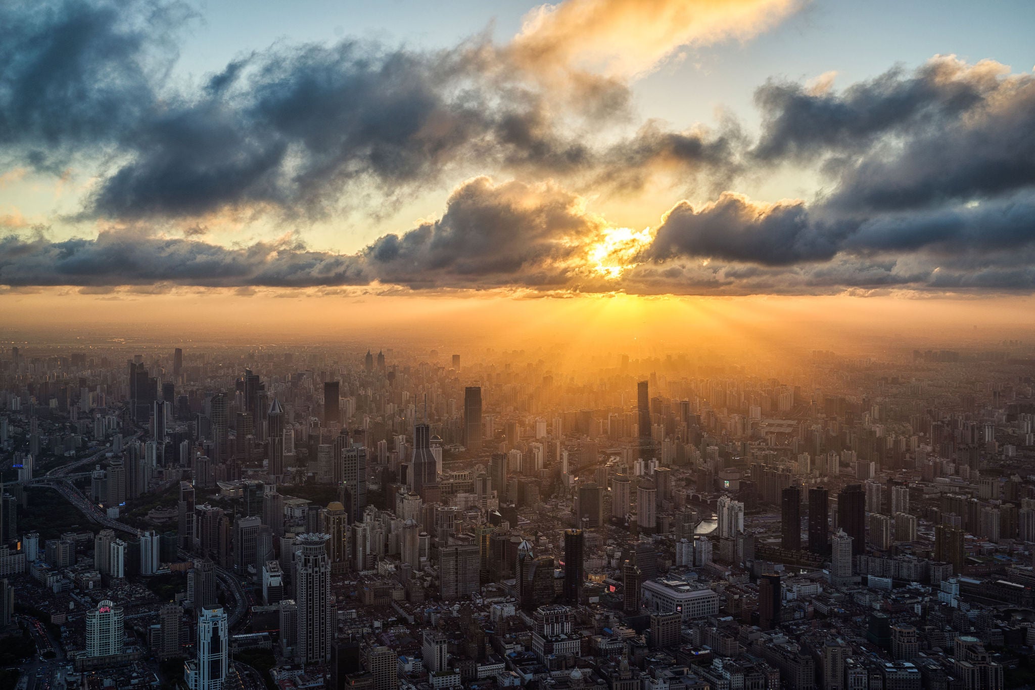 Die Morgensonne bricht durch Wolken und beleuchtet eine dichte Großstadt mit zahlreichen Hochhäusern
