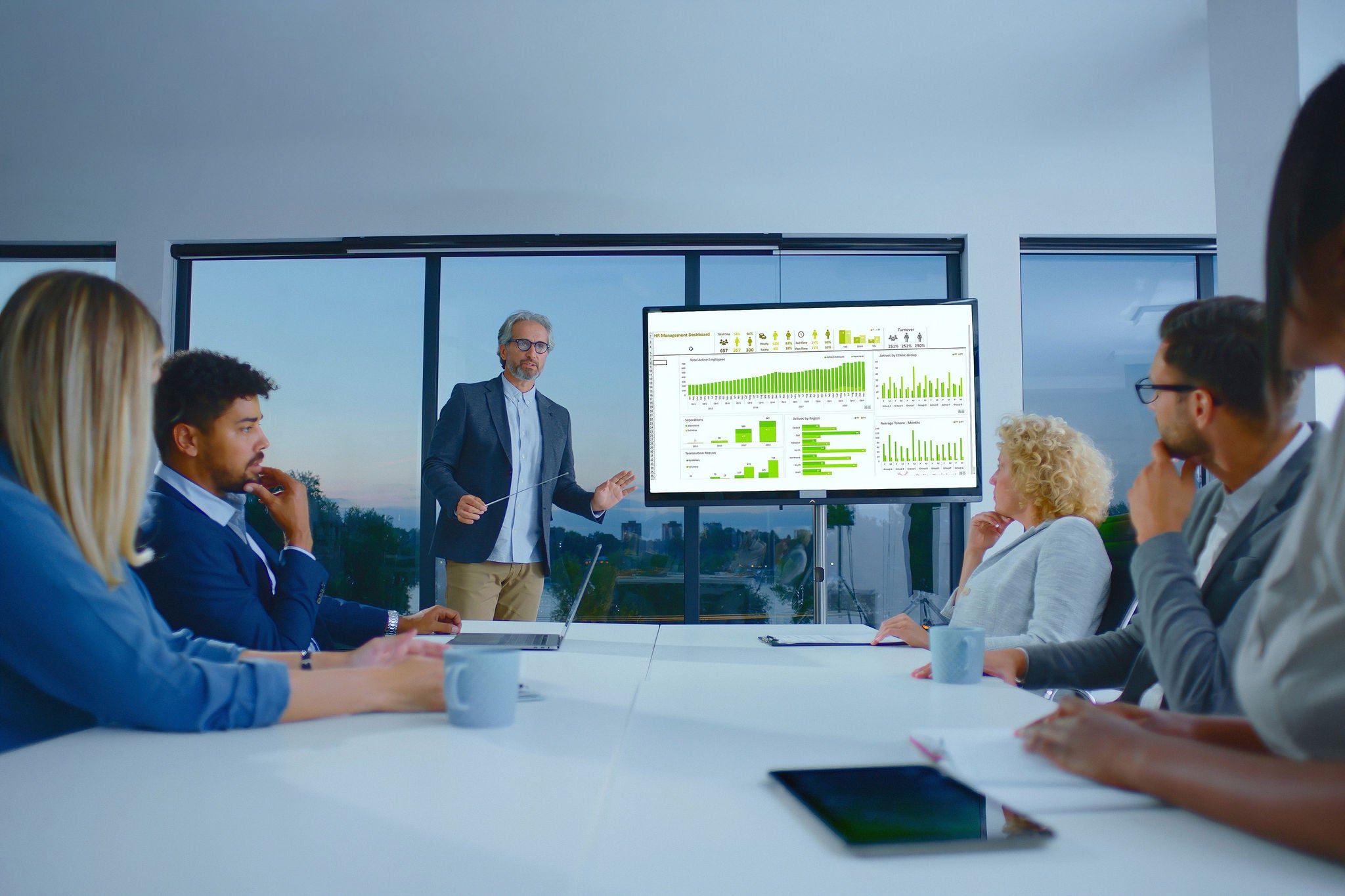 Confident businessman presenting financial data and charts on a large screen to a diverse team of colleagues