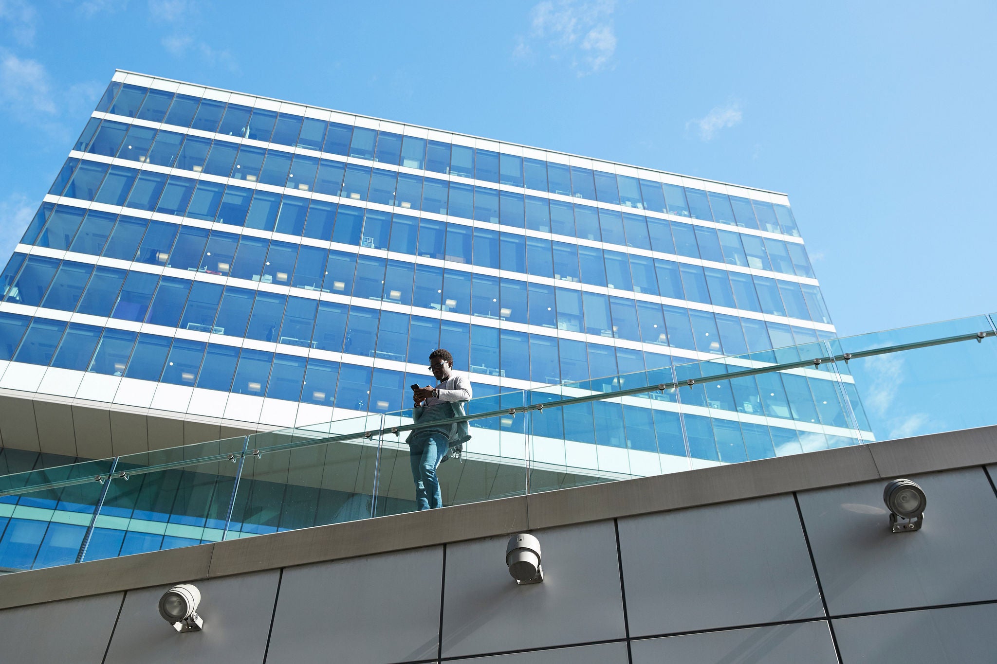 Businessman using smart phone while standing by glass railing against office building