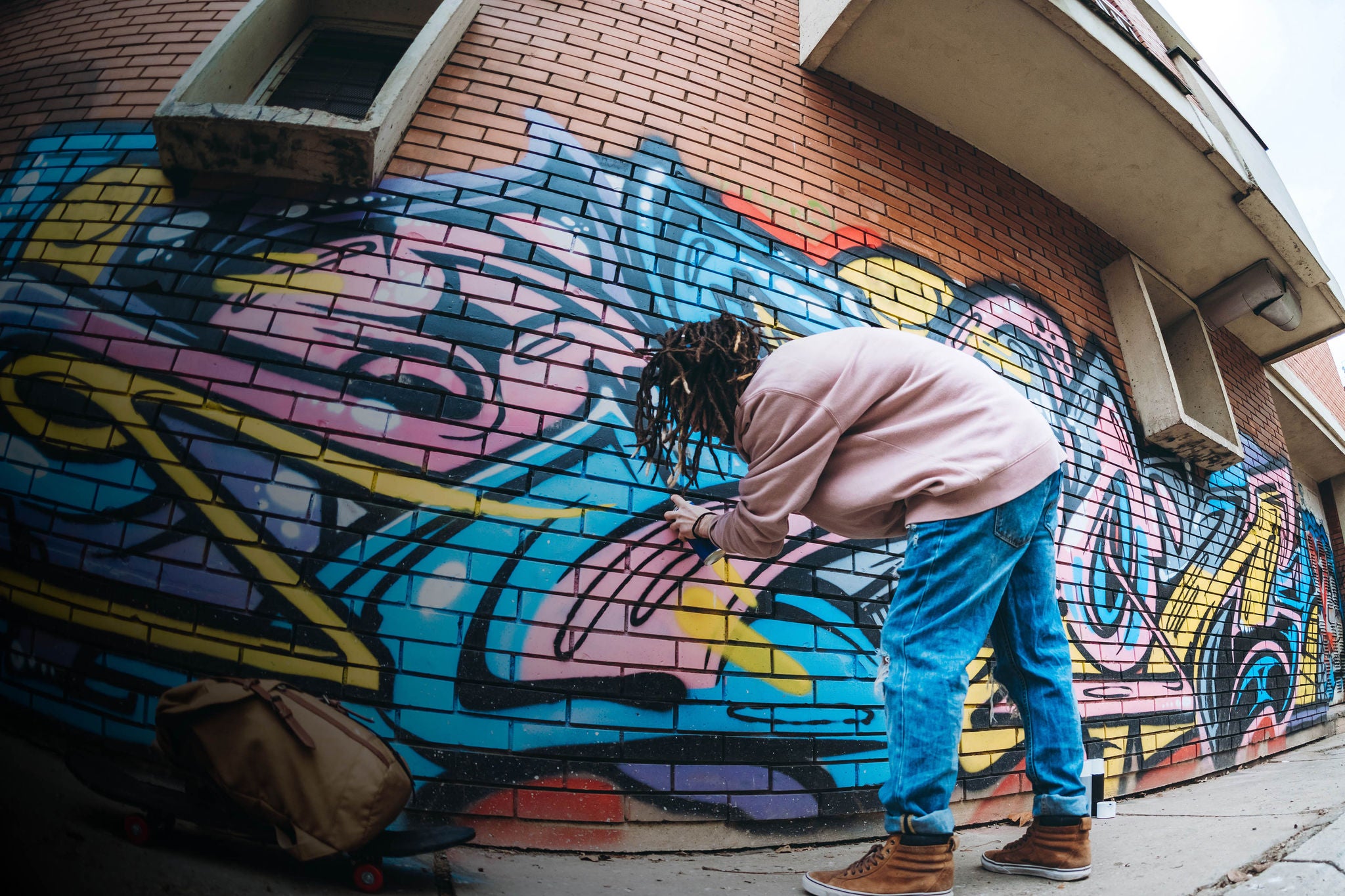 Young caucasian graffiti artist with dreadlocks painting graffiti.