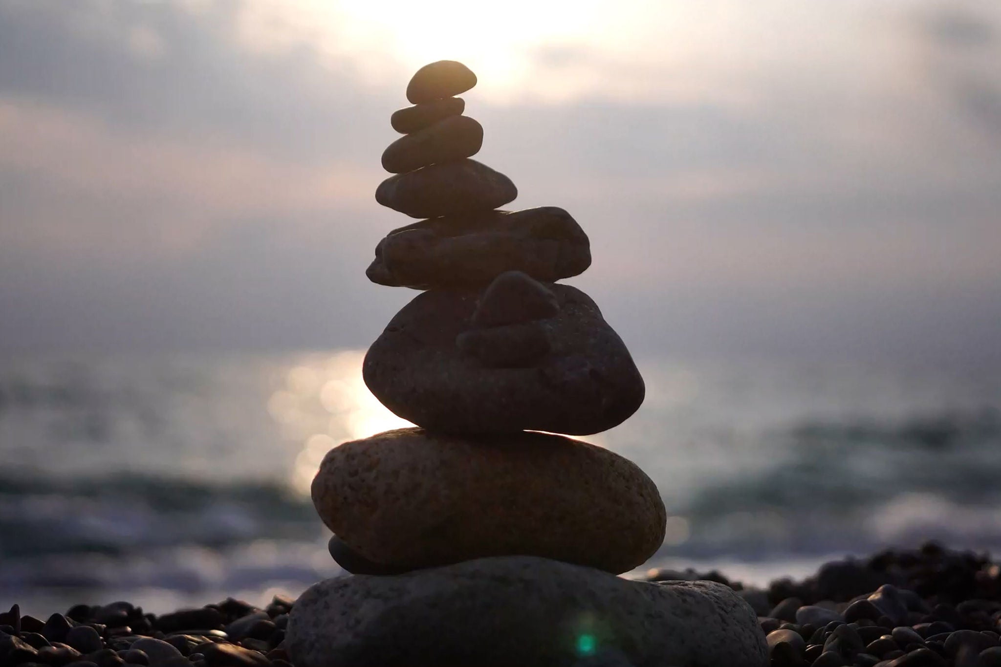 Balanced pebbles pyramid on the beach on cloudy day and clear sky at sunset
