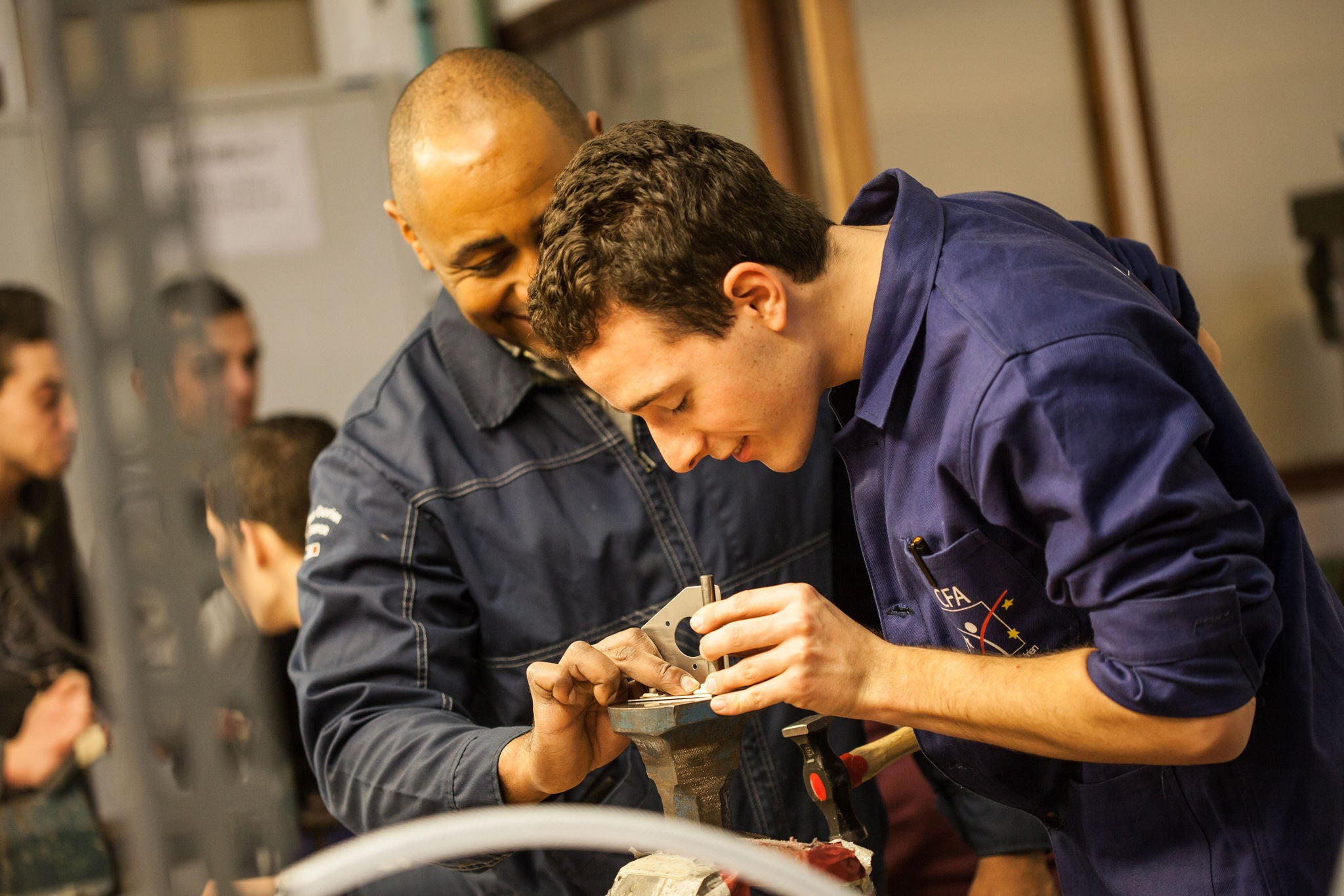 Formateur guide apprenti utilisant outil en atelier technique