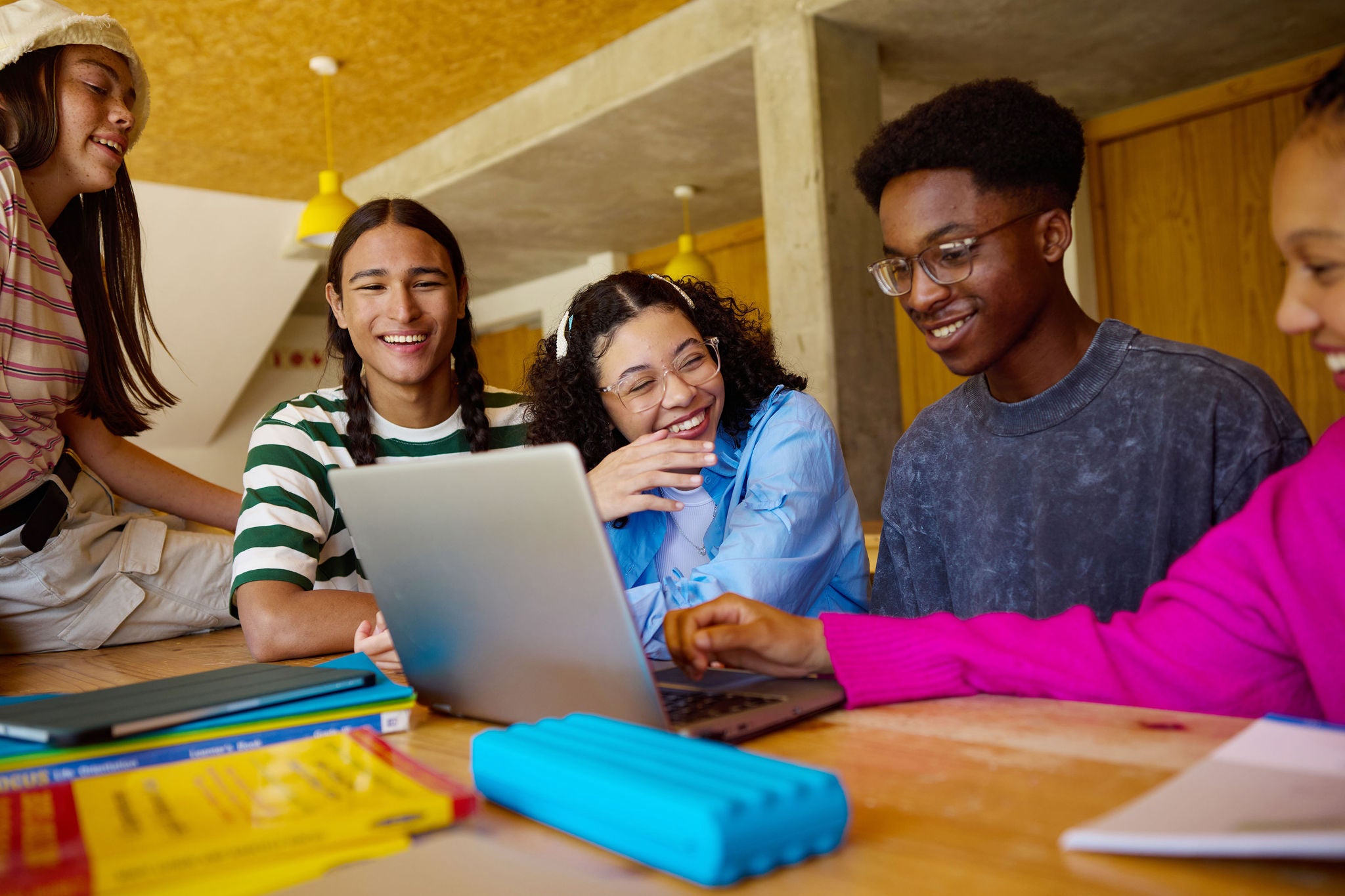 Diverse group of high school students working together on a school project, using a laptop in the library