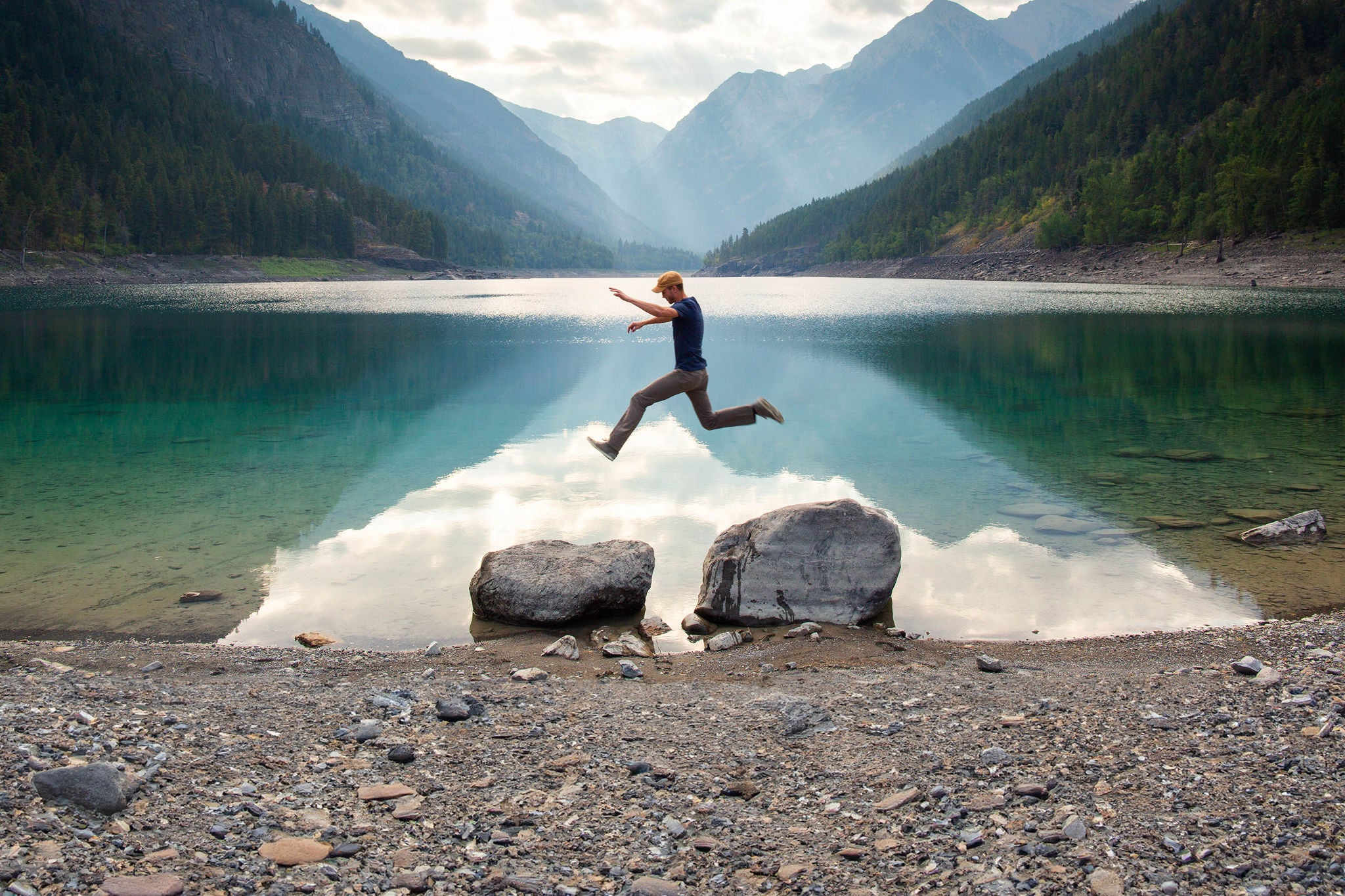 Man jumping between rocks by a lake with mountains