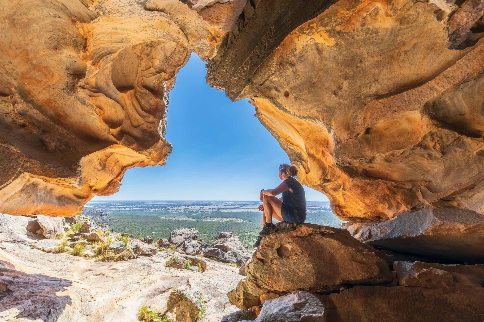 Frau sitzt in Felsenöffnung mit Blick ins Tal
