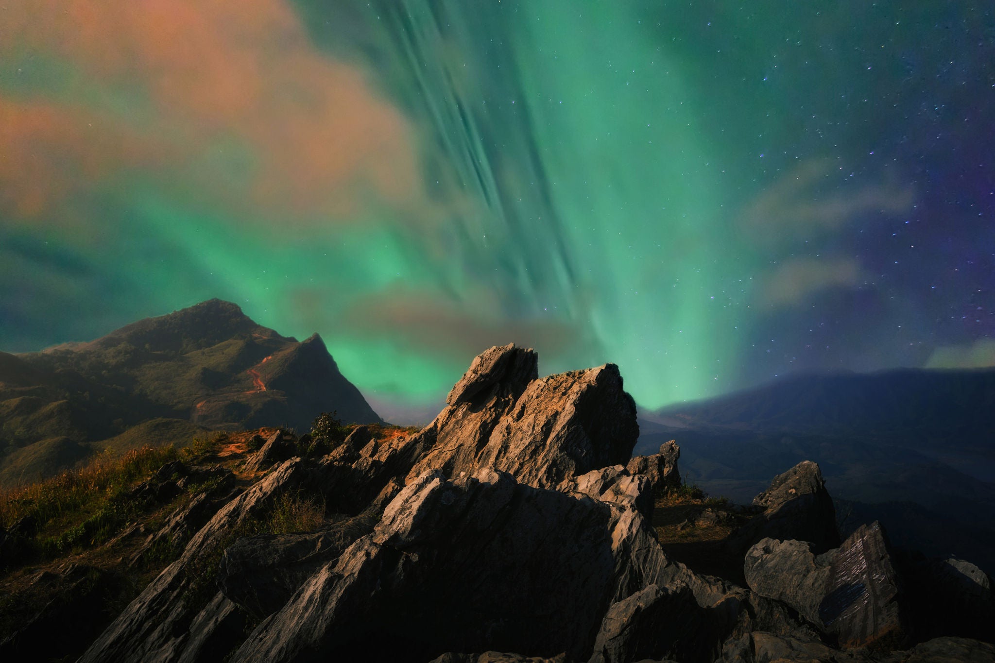Grønt nordlys over et dramatisk fjellandskap under en stjerneklar himmel