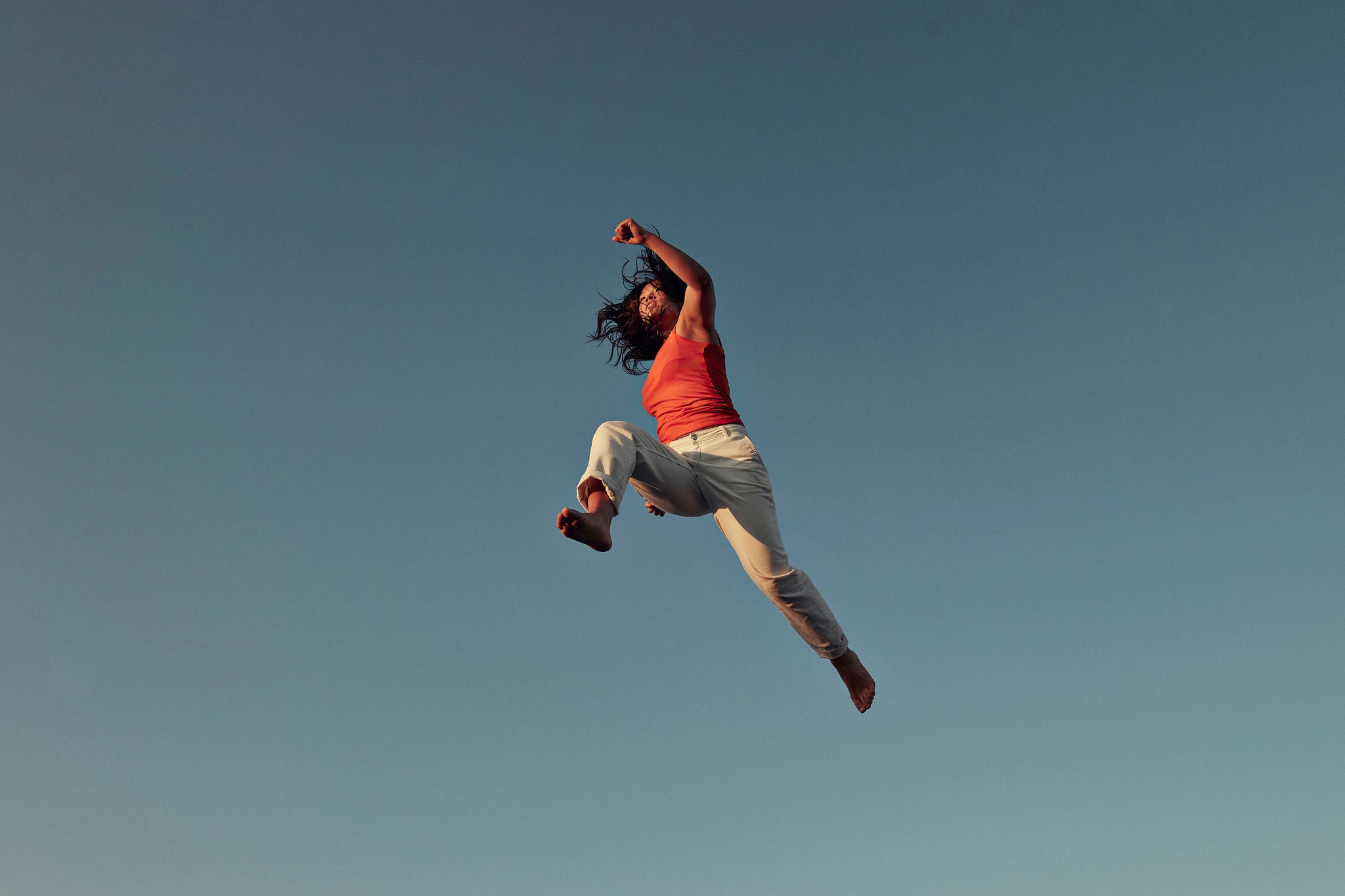 Person springt kraftvoll in der Luft vor blauem Himmel, Symbol für Energie und Freiheit