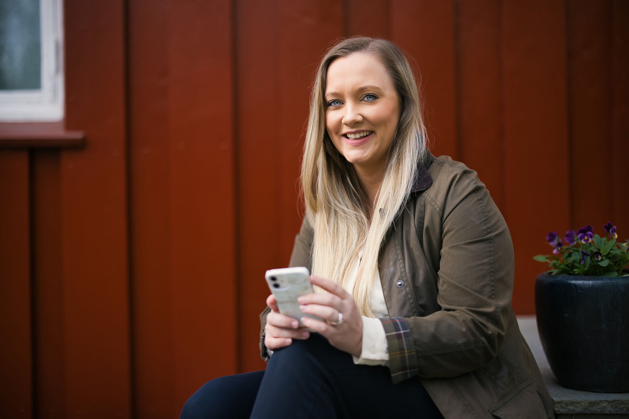 Gidske Leikvoll sitter på trappa smilende foran et rødt hust