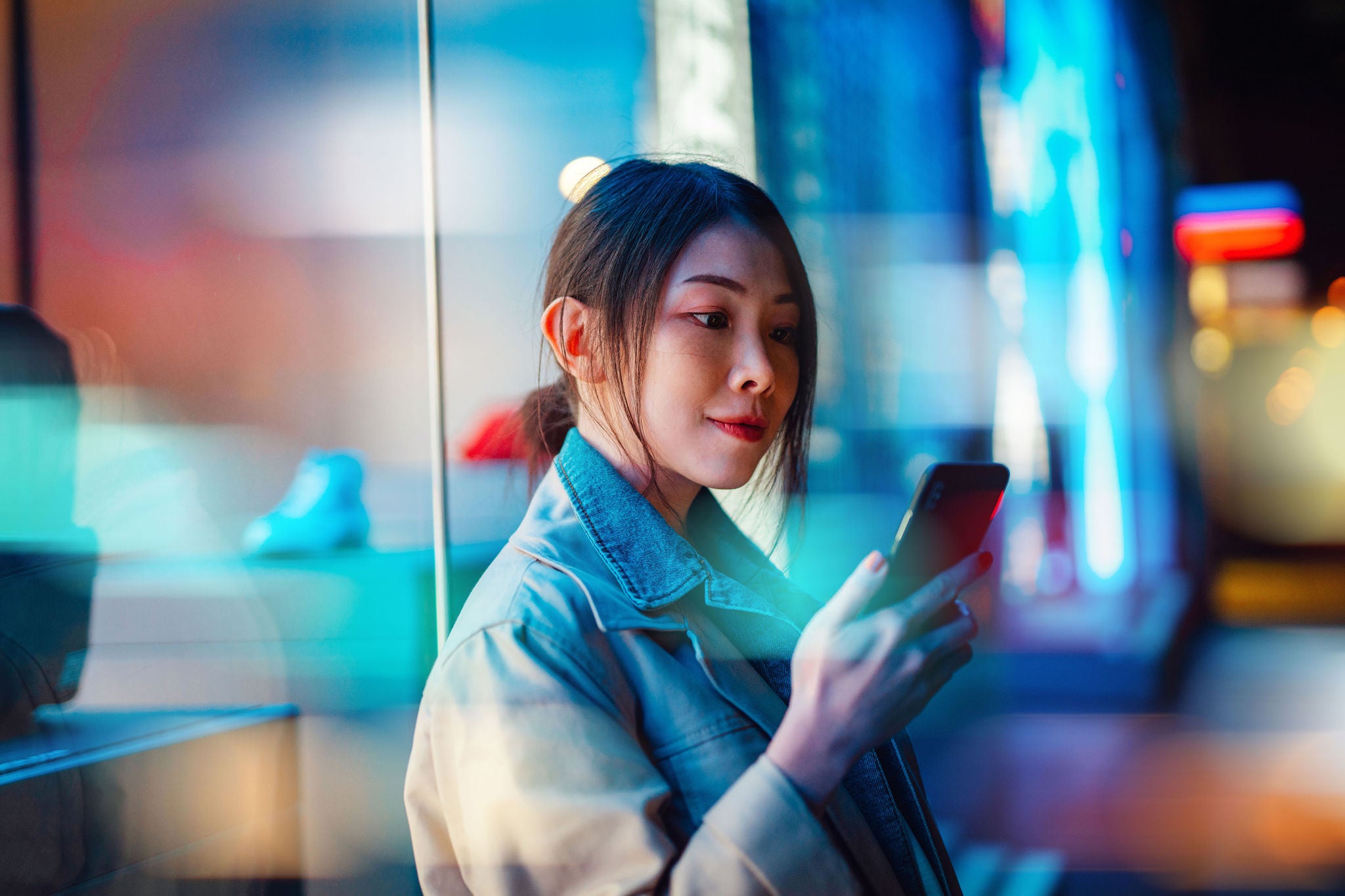 Side profile of a beautiful young Asian businesswoman using smartphone and walking on the street at night in the city.